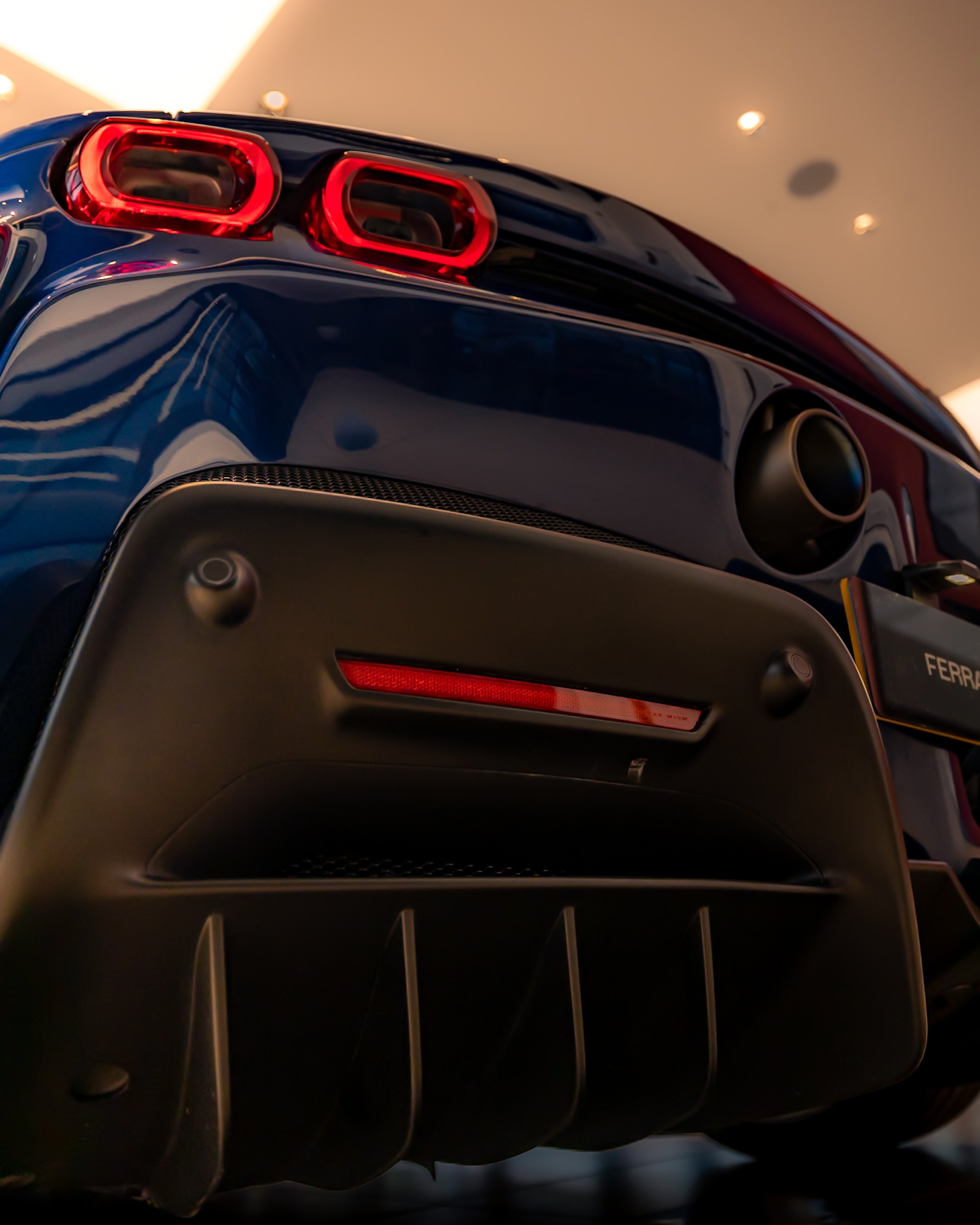 Close-up of a blue sports car's rear with red taillights and a visible exhaust pipe, showcasing the design details of the bumper and diffuser.