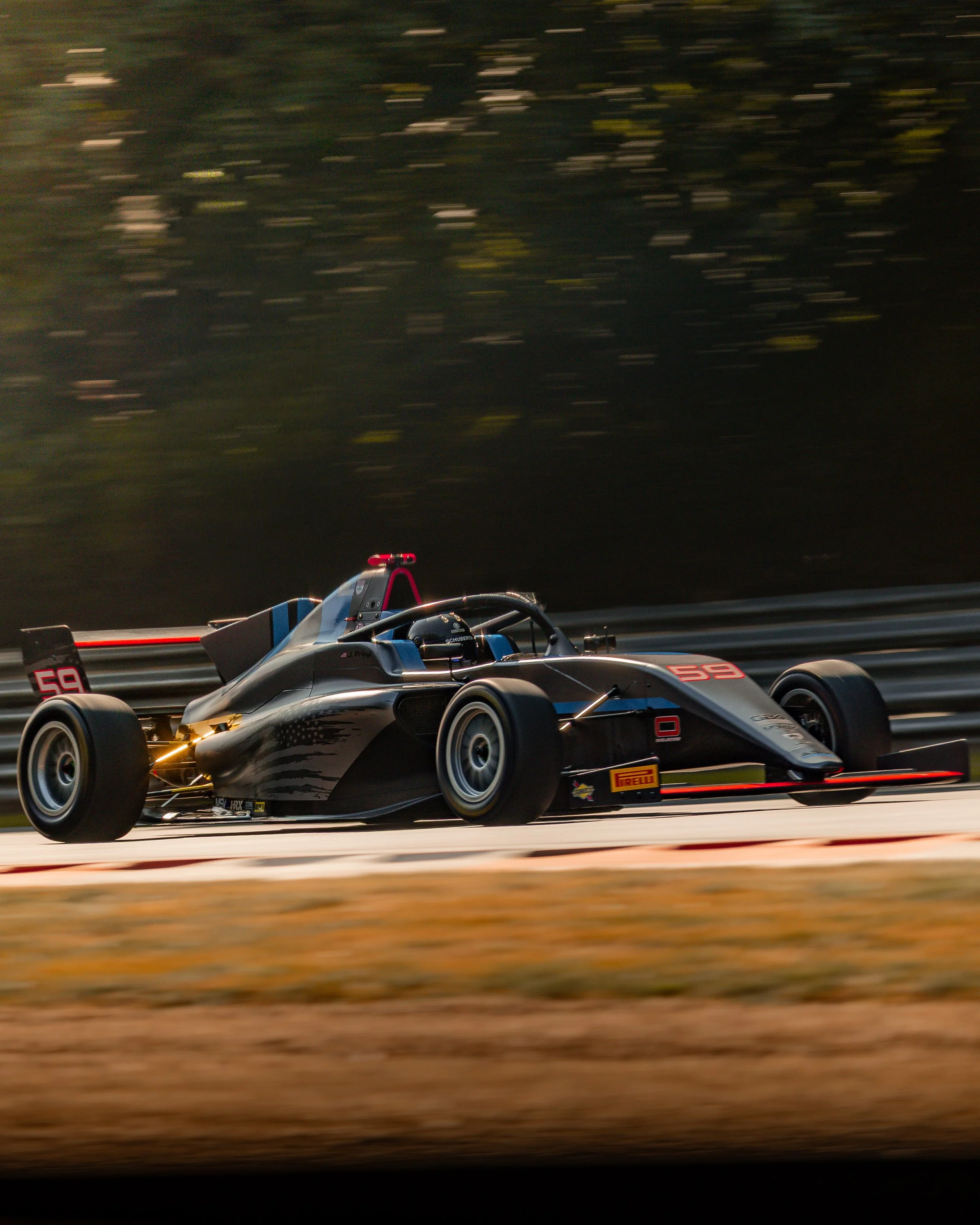 A black and blue race car speeding on a track, with trees blurred in the background.