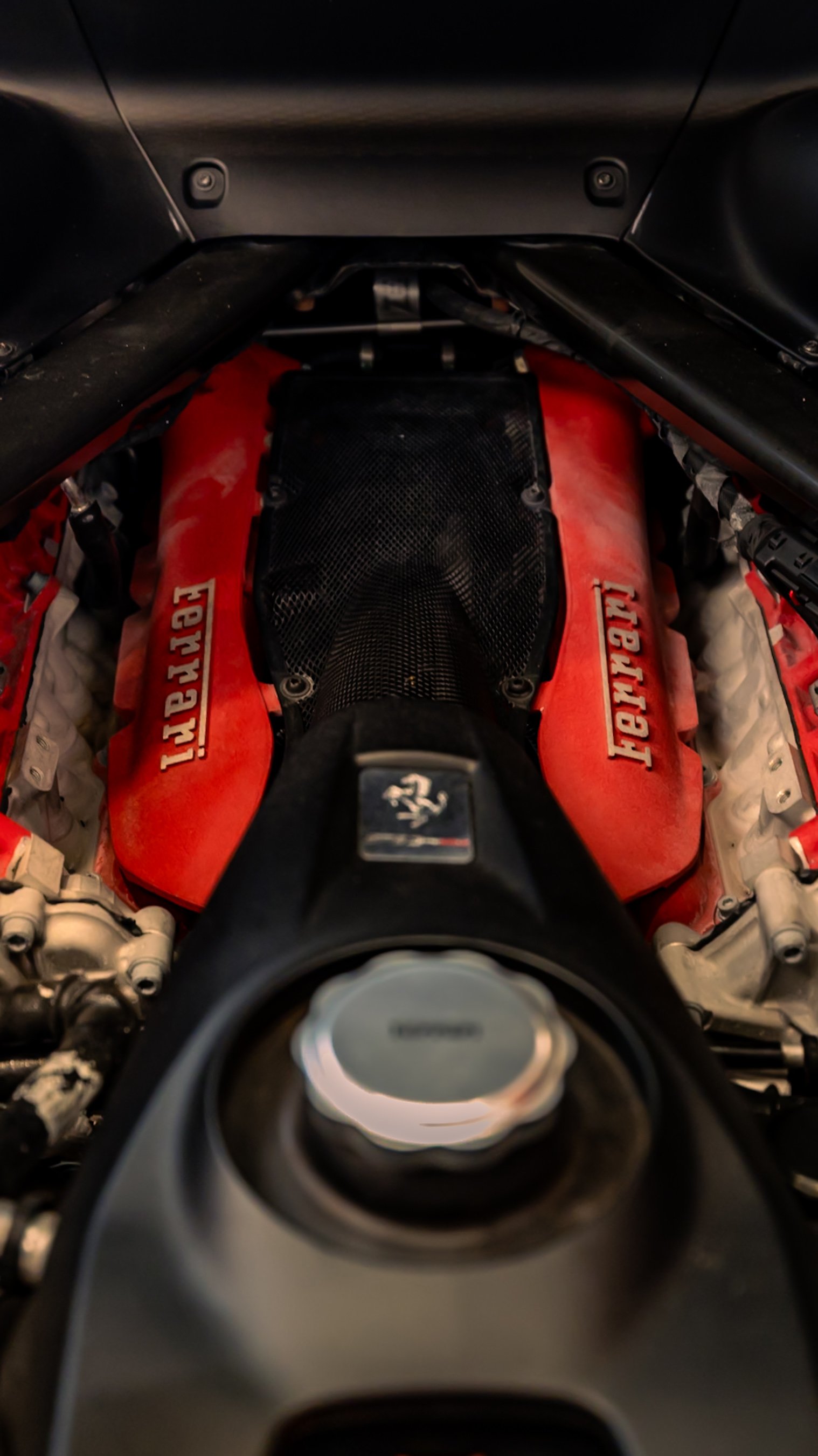 Ferrari engine with red covers and Ferrari logo, showing complex mechanical components inside a car.