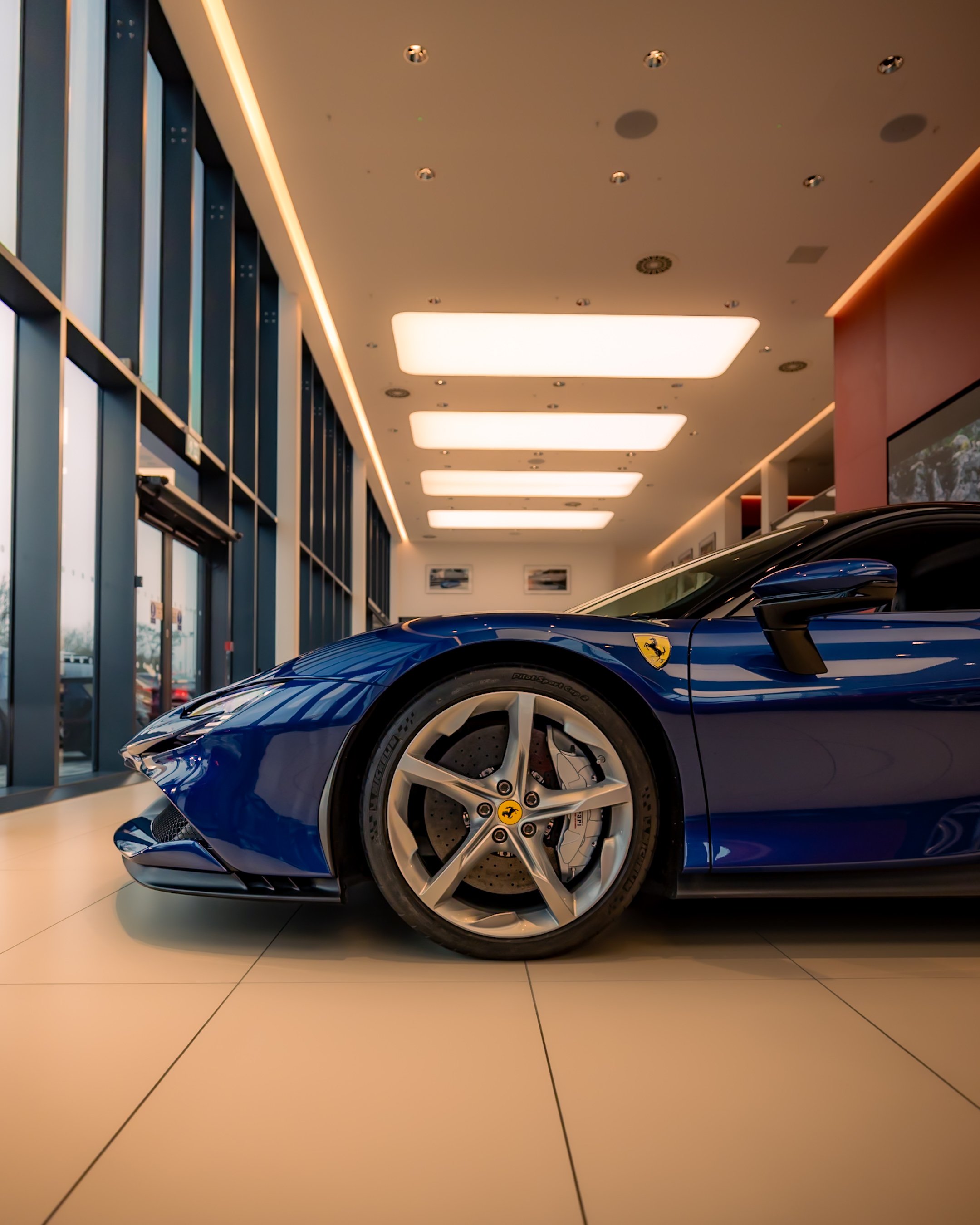 Side view of a blue luxury sports car in a modern showroom, focusing on the front wheel and part of the car's body.