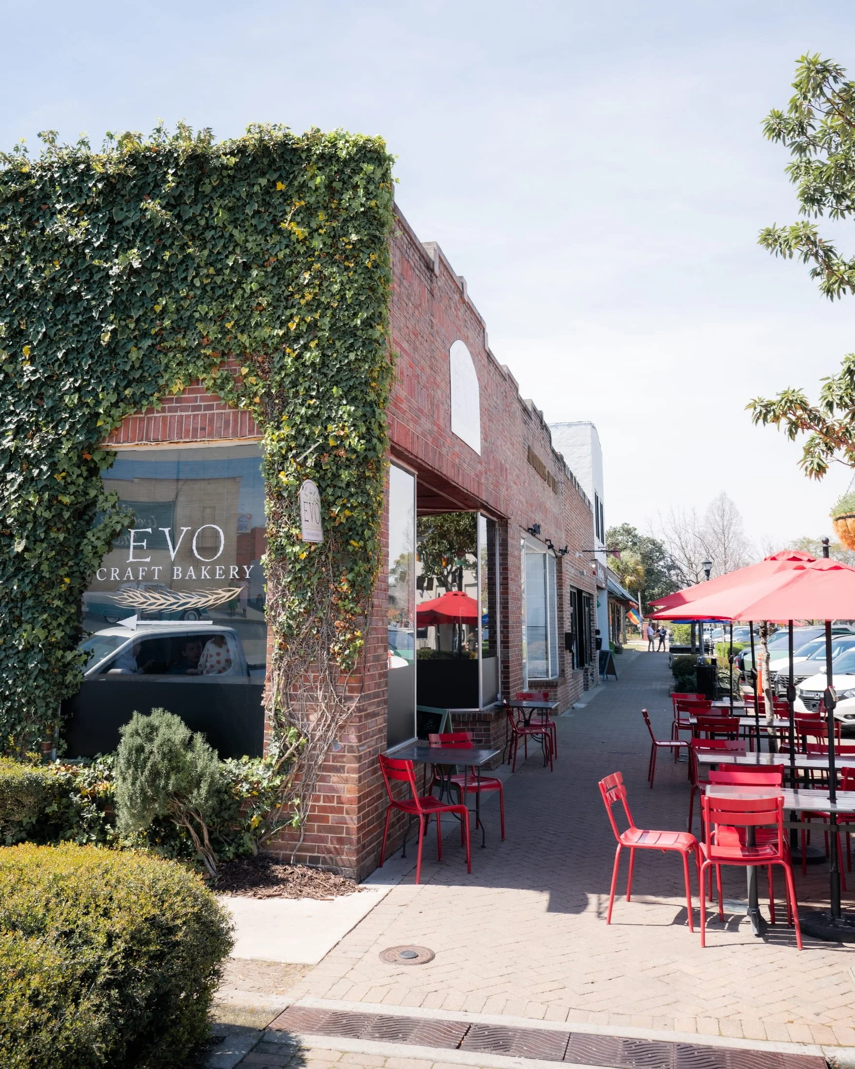 Park Circle outdoor seating area with red chairs and tables under red umbrellas outside a brick building with ivy growing on the wall.