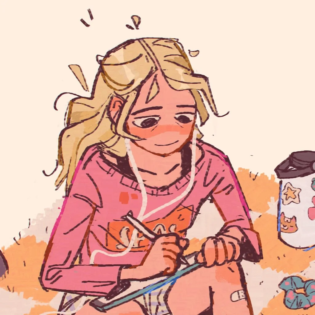 A girl with long blonde hair wearing a pink sweater, sitting at a desk, writing or drawing on a notepad. She appears focused and is possibly listening to music with headphones. There is a black cup with star and moon designs on it and some crumpled papers nearby.