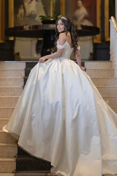 Bride in a voluminous white ball gown with a beaded bodice and tiara poses on a grand marble staircase.