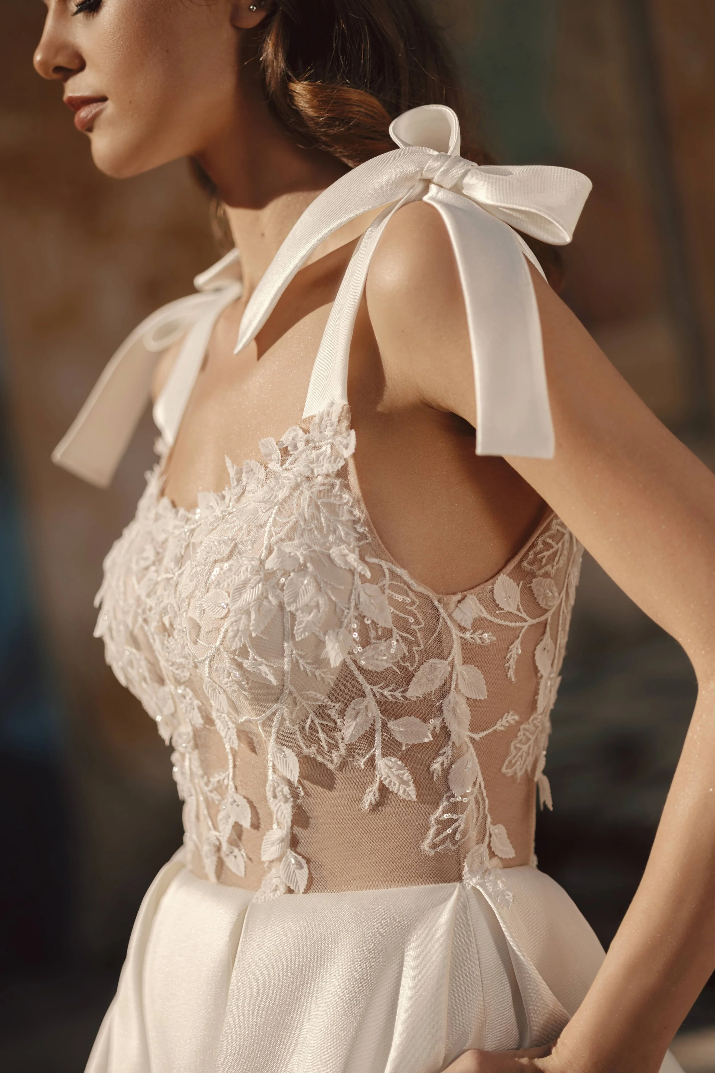 A woman wearing a white lace dress with large shoulder bows, standing in warm light with one hand at her waist.A woman wearing a white lace dress with large shoulder bows, standing in warm light with one hand at her waist.