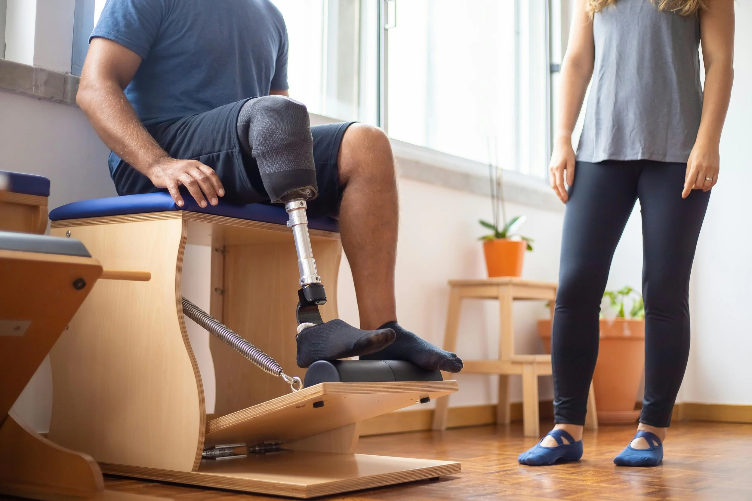 A man with a prosthetic leg sits on an exercise bench while the physical therapist watches to the side.