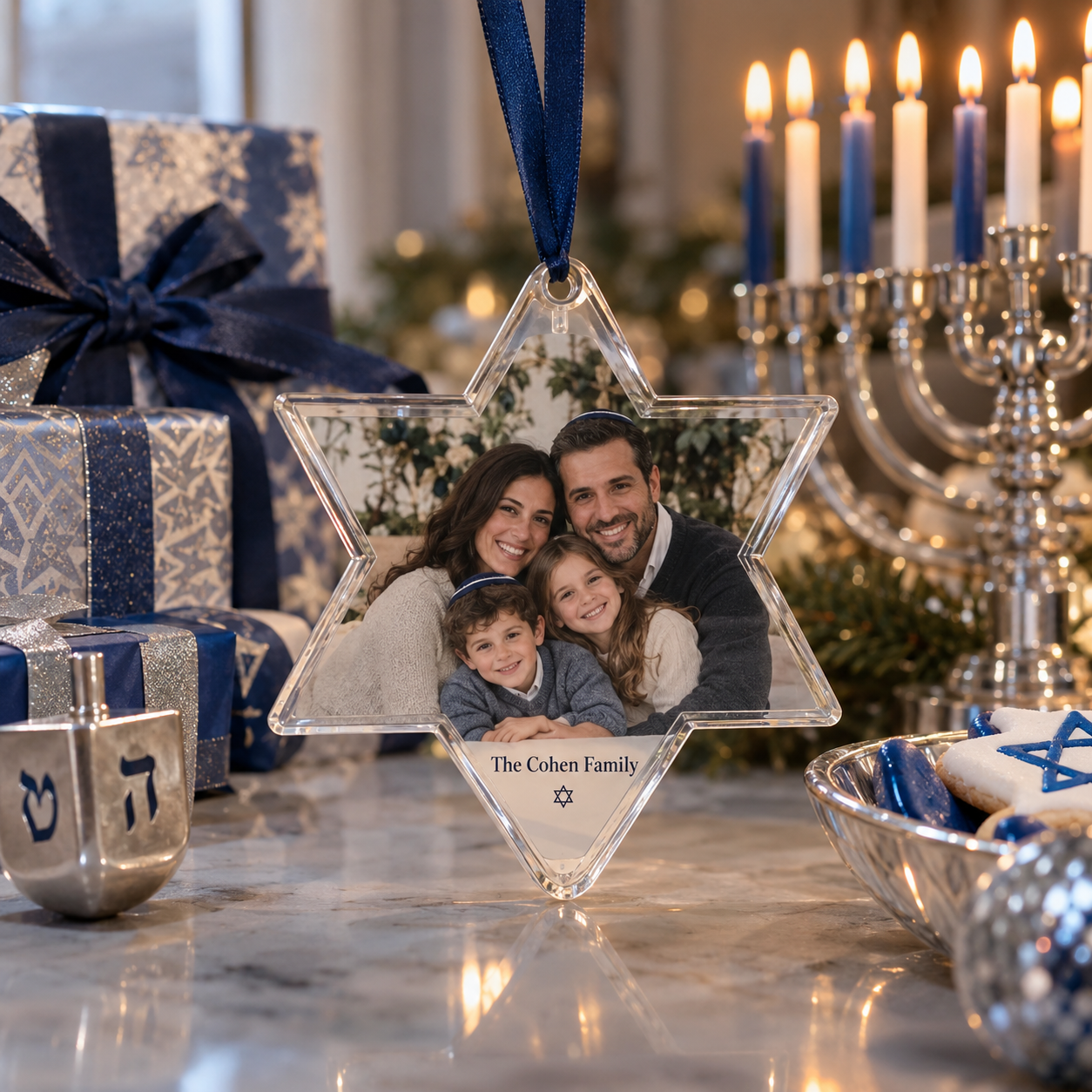 A Christmas ornament with a family photo of four smiling family members, labeled 'The Cohen Family' with a Star of David symbol, surrounded by holiday decorations including wrapped presents, a menorah with lit candles, and a bowl of decorated cookies.
