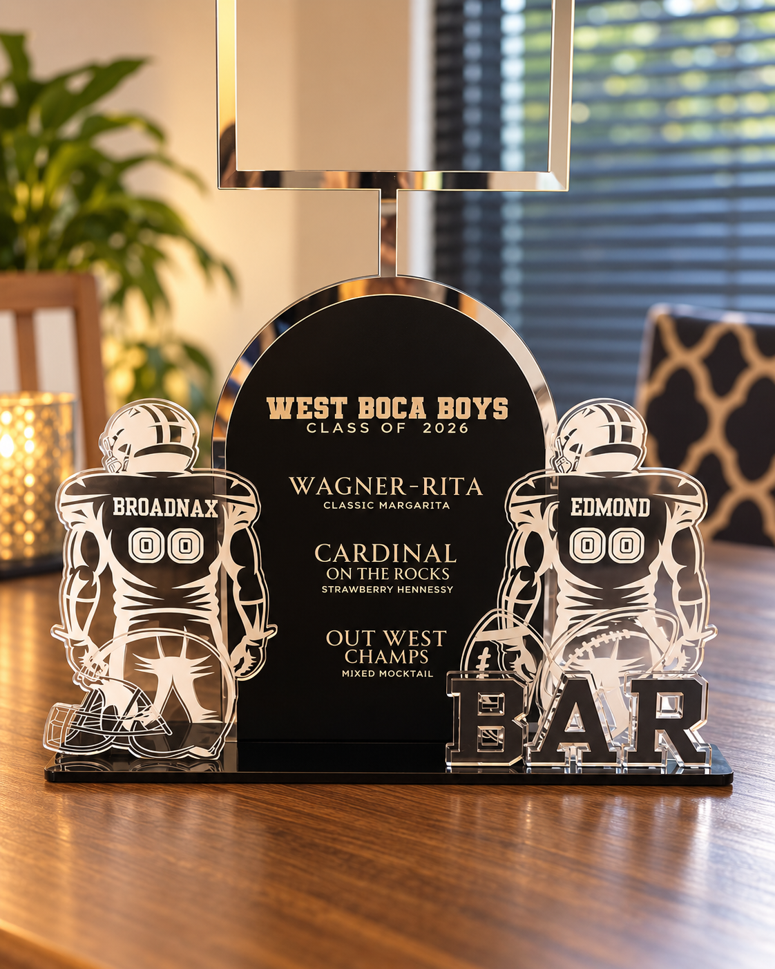 Decorative sign celebrating West Boca Boys Class of 2026 graduates, featuring football player cutouts with names Broadnax and Edmond, and a bar prompt in the foreground.