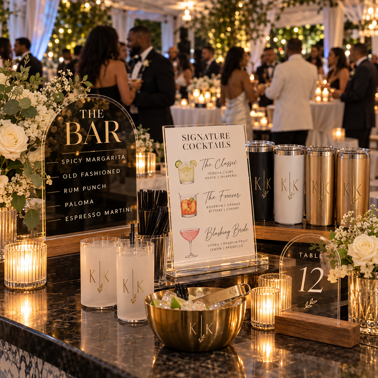 Decorated wedding reception bar with cocktail menu, candles, floral arrangements, and guests in formal attire in the background.