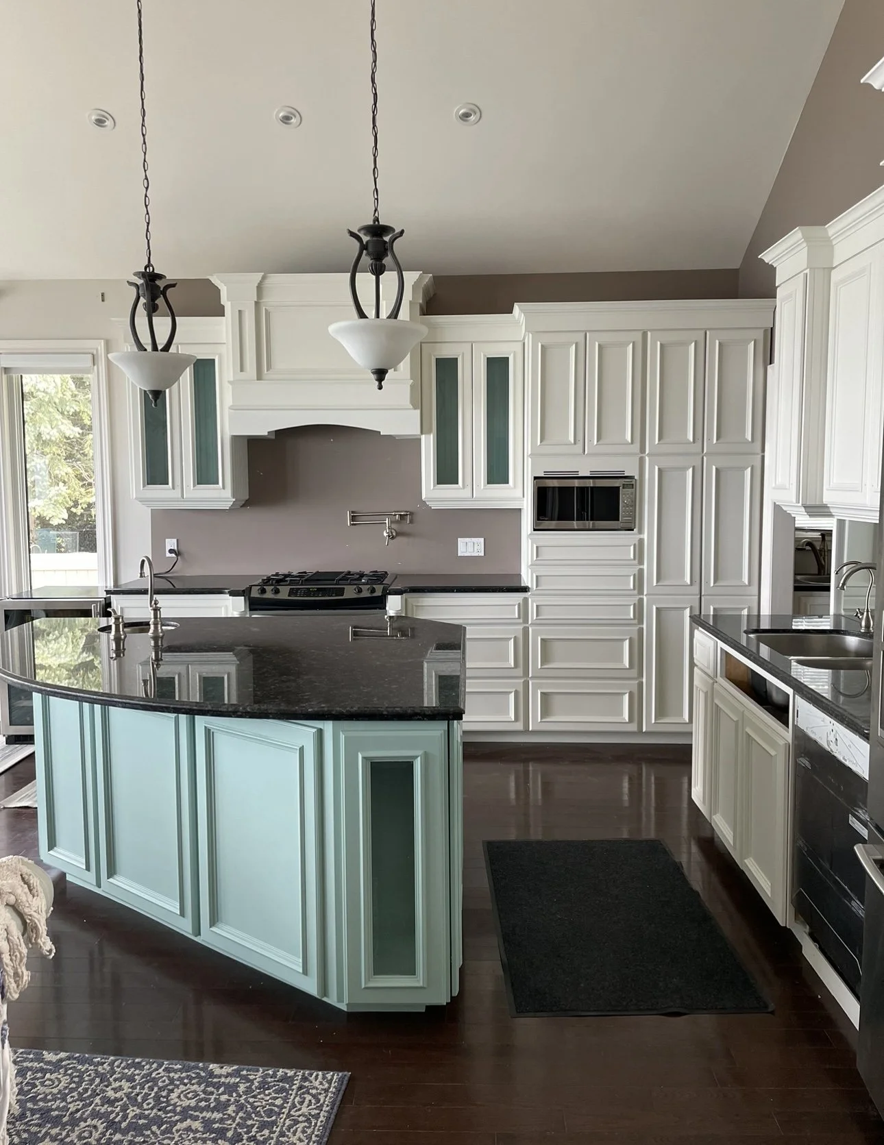 Modern kitchen with white cabinetry, a turquoise island with black countertop, pendant lights, a gas stove, and a built-in microwave.
