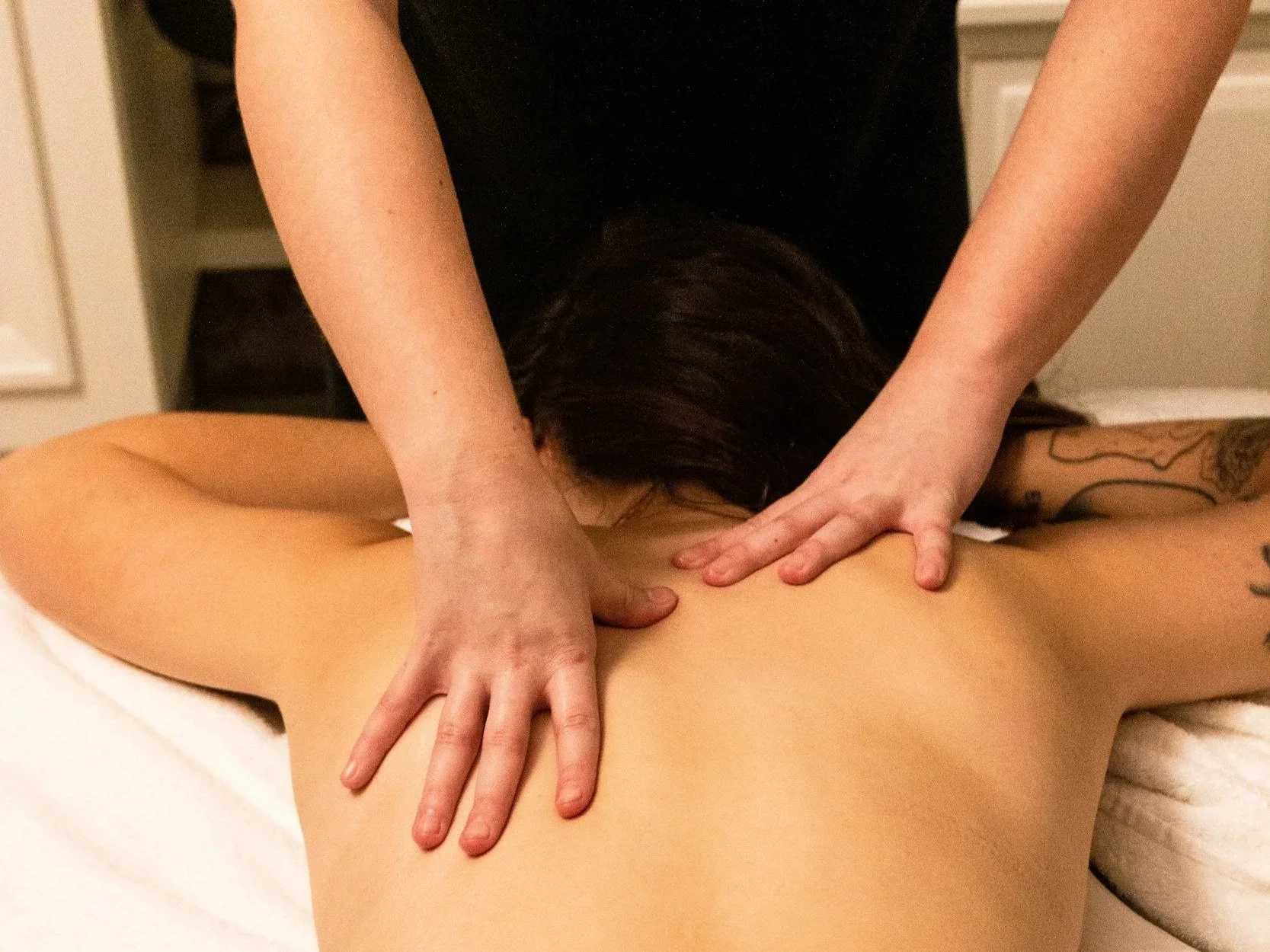 A person receiving a massage on their back from a massage therapist in a spa or therapy room.