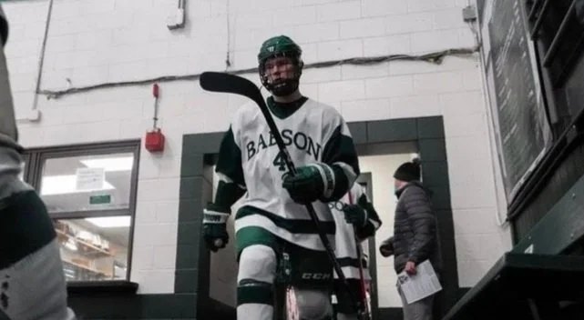 Hockey player in a green and white uniform with hockey stick in an indoor sports facility.