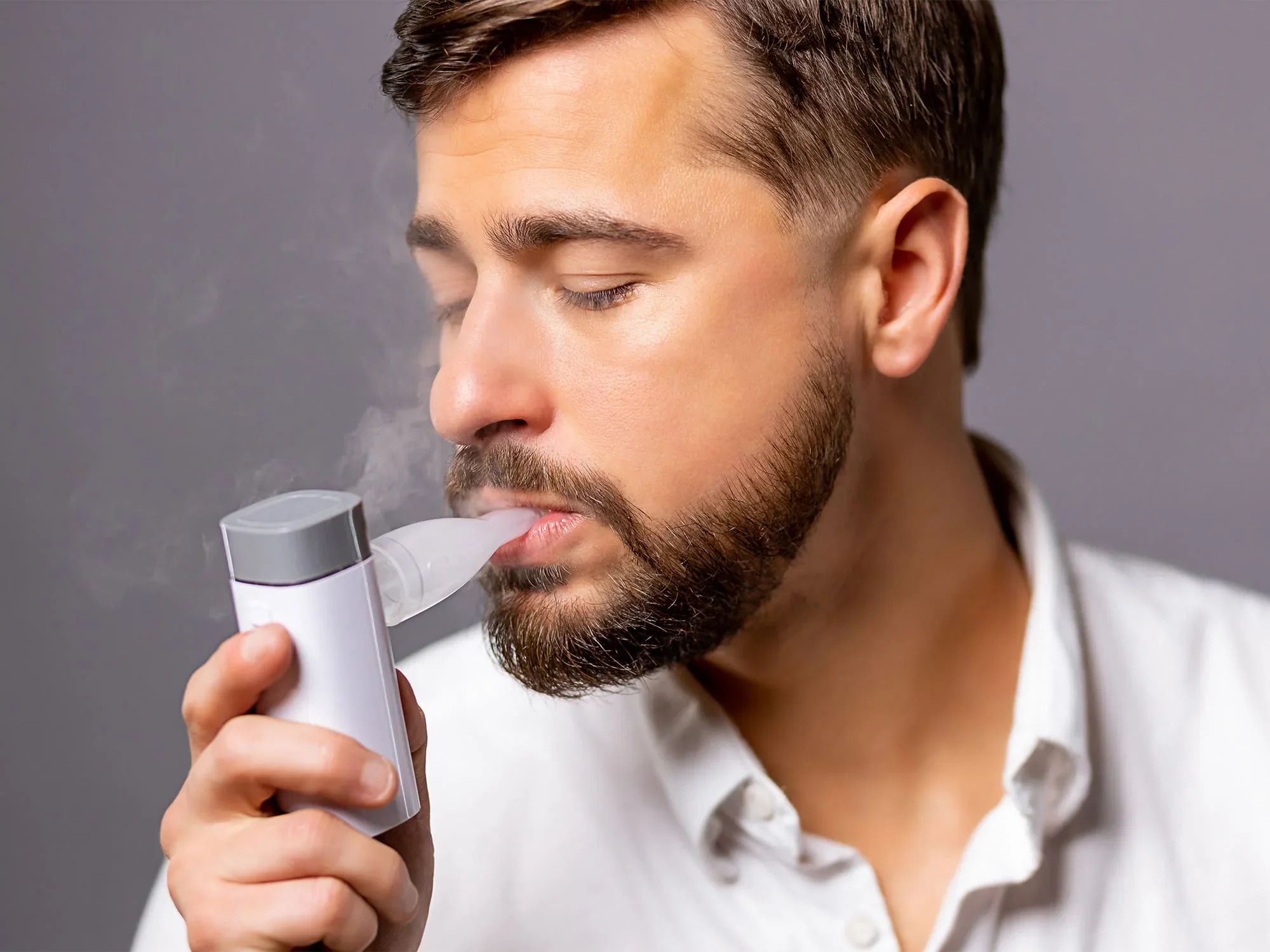 A man with a beard using an electronic vaporizer or vape pen.