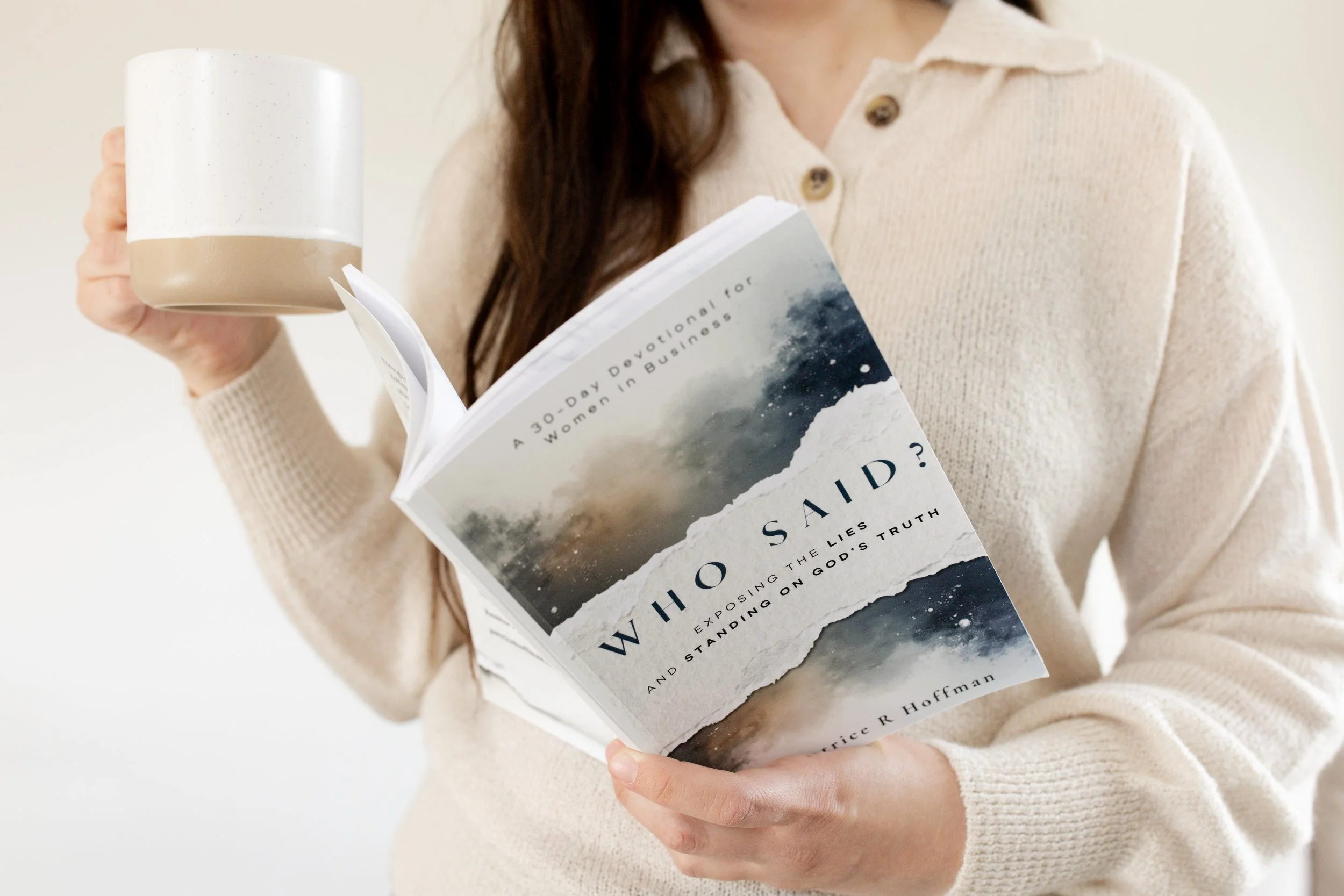 Person holding a coffee mug in one hand and a book titled 'Who Said?' in the other, wearing a cream-colored sweater.