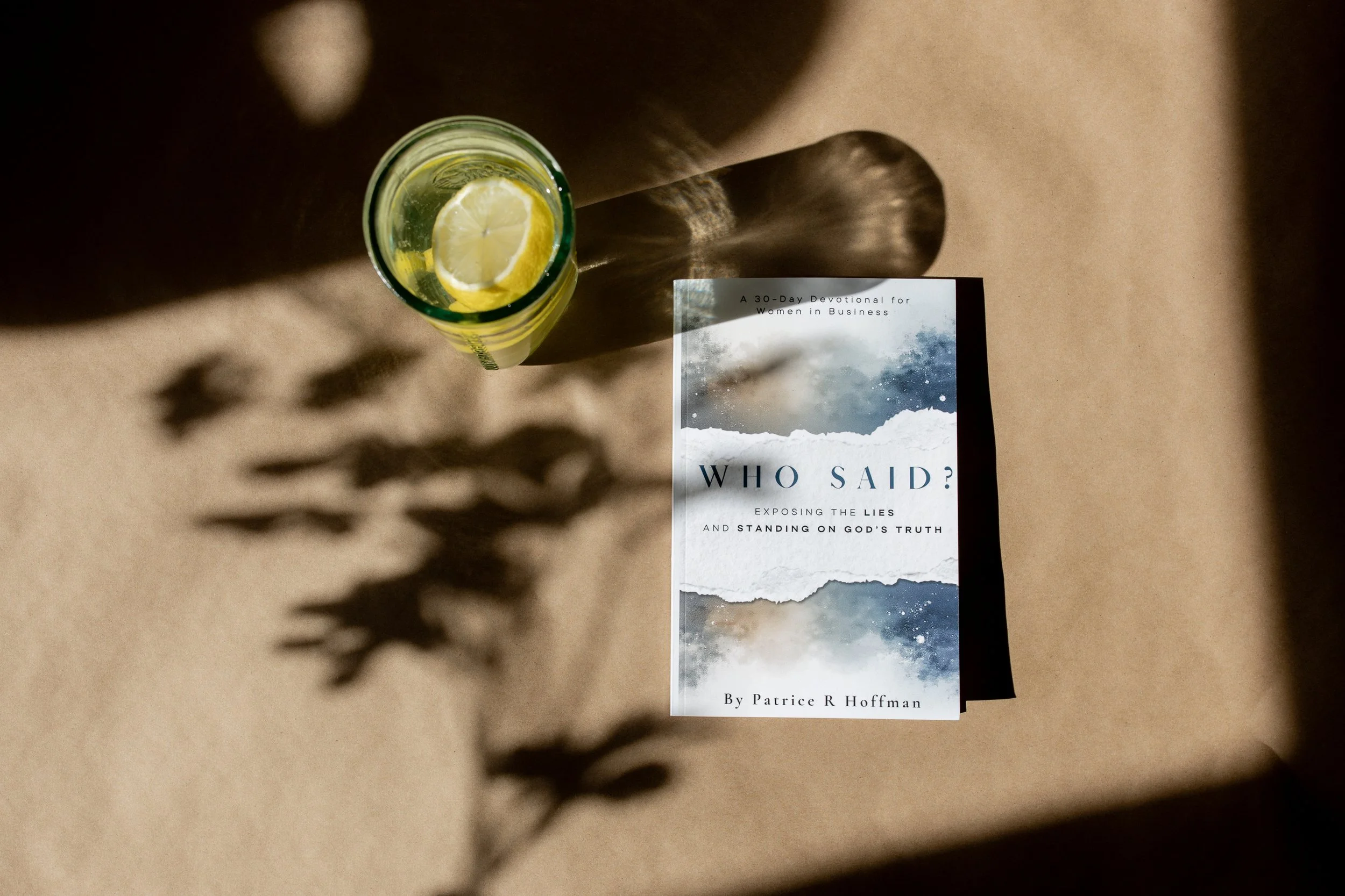 A book titled 'Who Said? Exposing the Lies and Standing on God's Truth' by Patrice R Hoffman. A glass of lemon-infused water casting shadows on a beige surface.