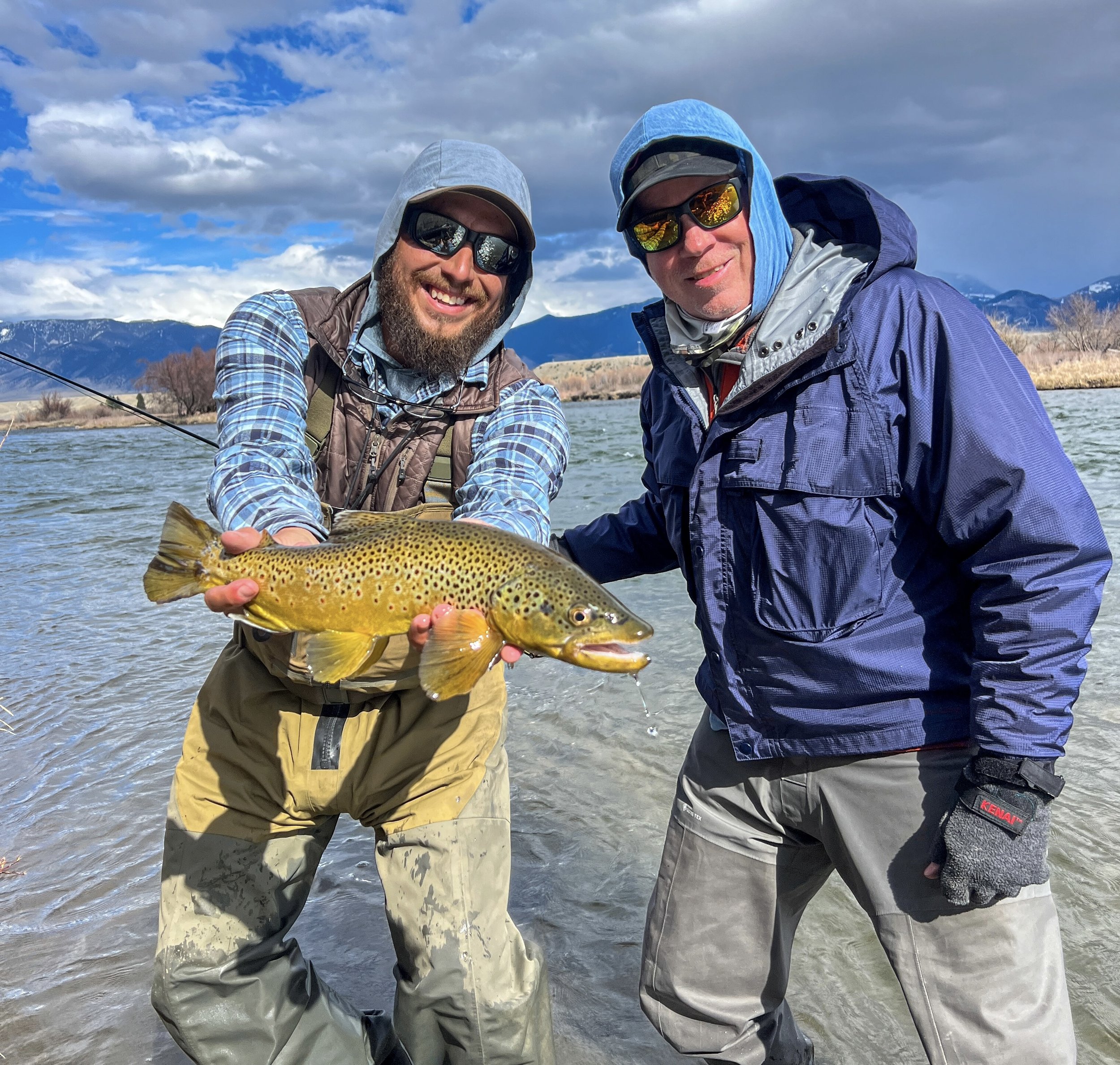 fishing guide holding a brown trout that the client standing next to him caught. on the upper madison river in montana