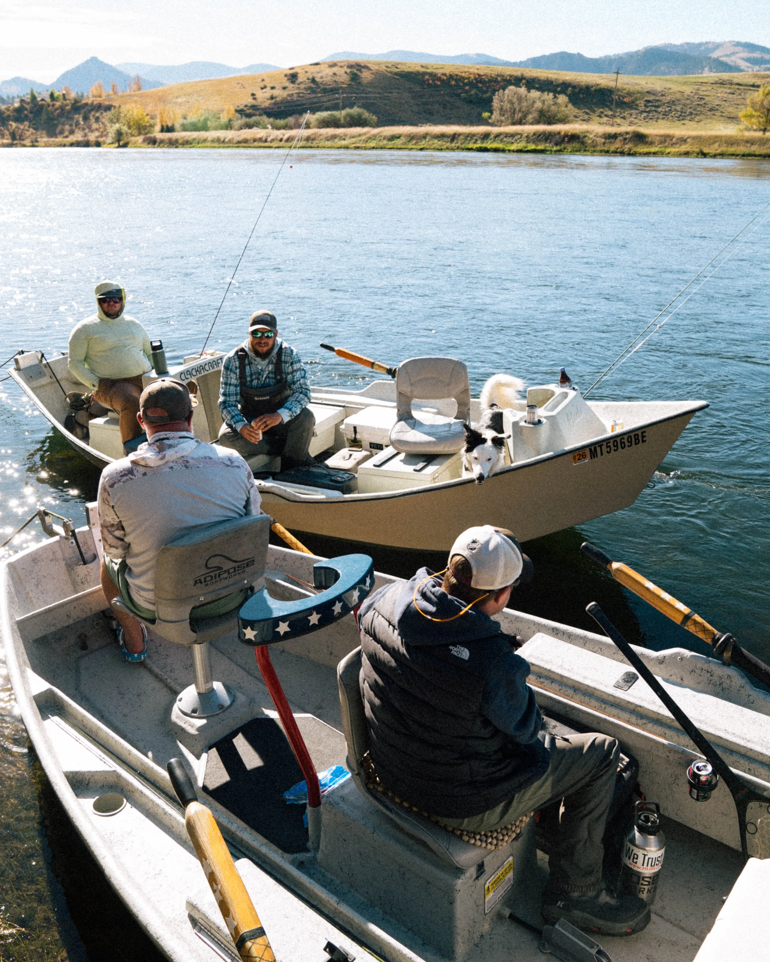 Four men and two dogs on two boats on a lake, with a hilly landscape in the background.