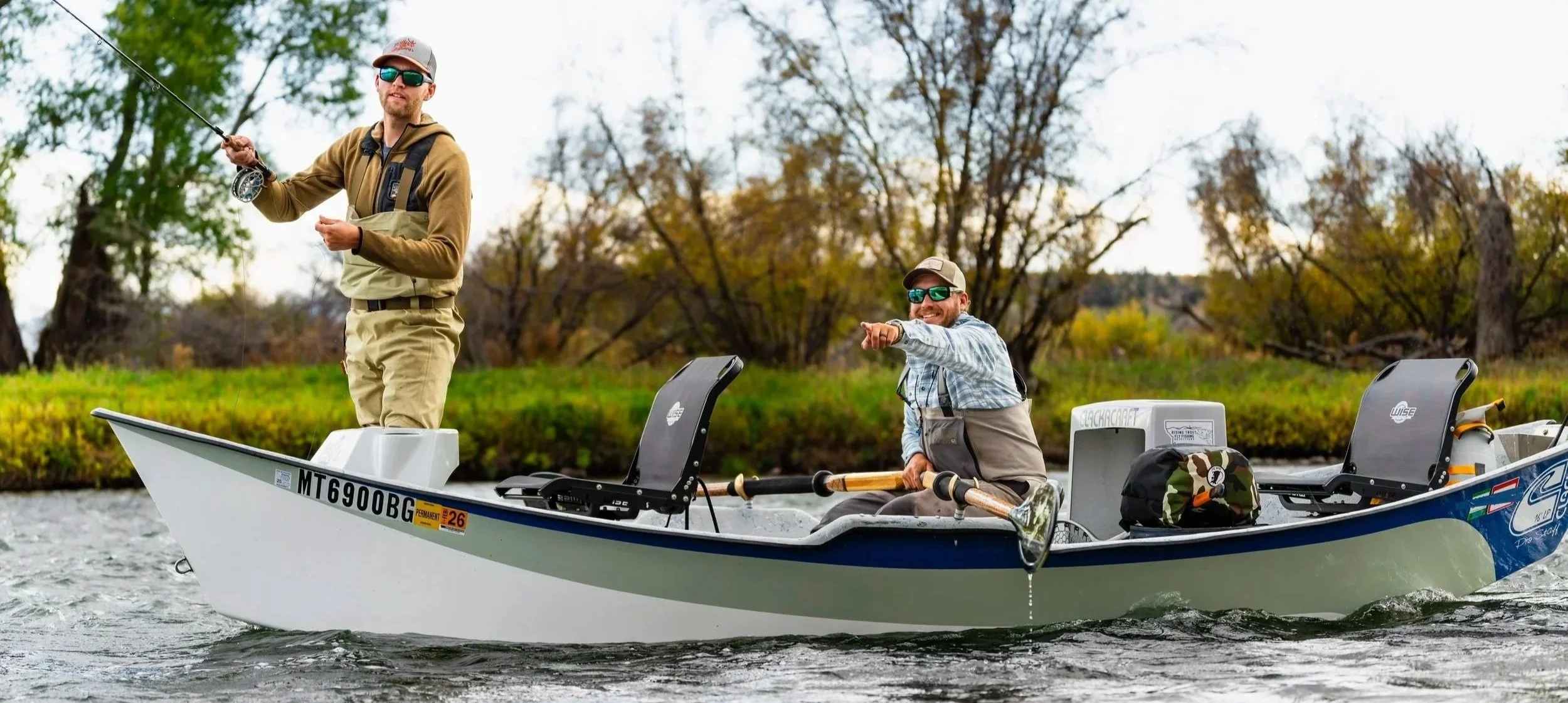 Angler casting out of the front of a drift boat on the Madison river in Ennis Montana as a guide from Rising Trout Fly Fishing Outfitters rows the boat and points where the client should cast