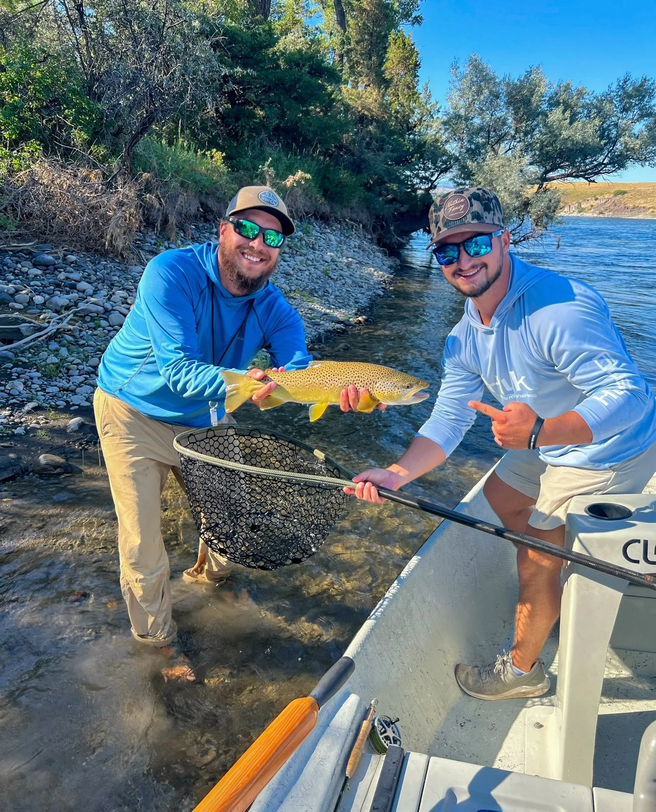 A fishing guide from Rising Trout Fly Fishing Outfitters holding a wild brown trout for a client on a guide trip on the yellowstone river in Montana