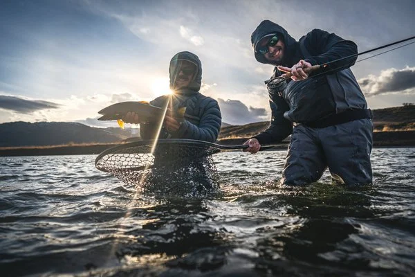 client holding a fish next to a fishing guide holding a net.