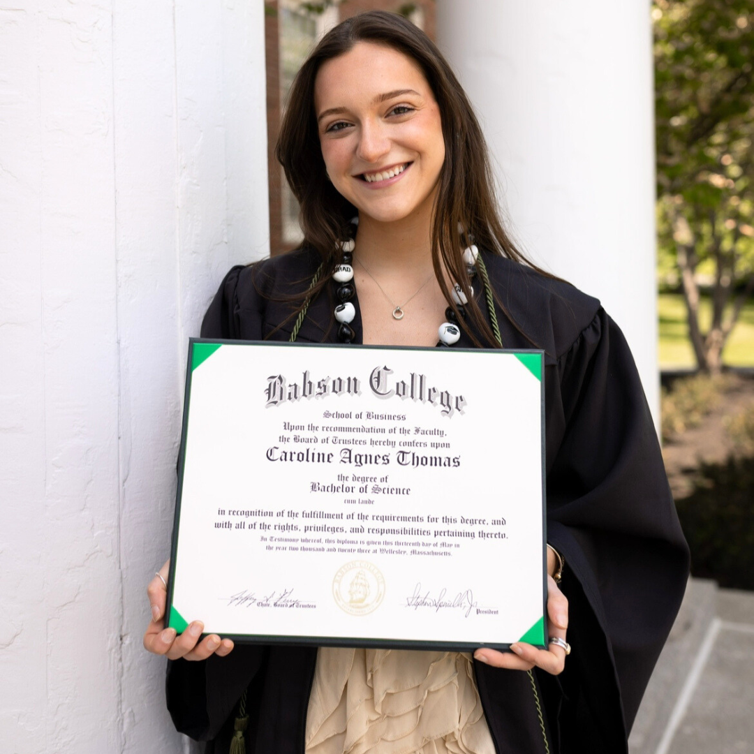 Person wearing graduation gown holding a diploma outdoors
