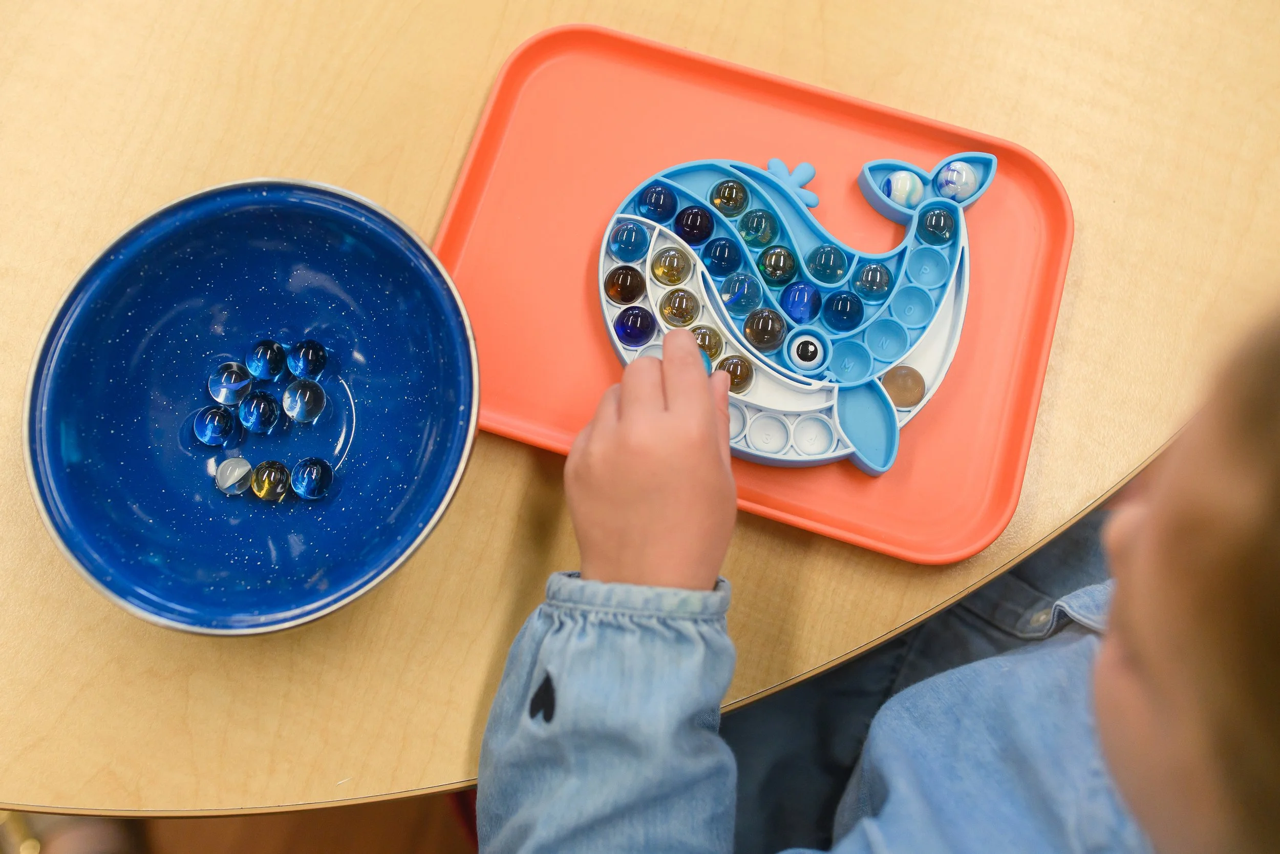 Children playing a marble game with a fish-shaped game board and marbles on a wooden table.