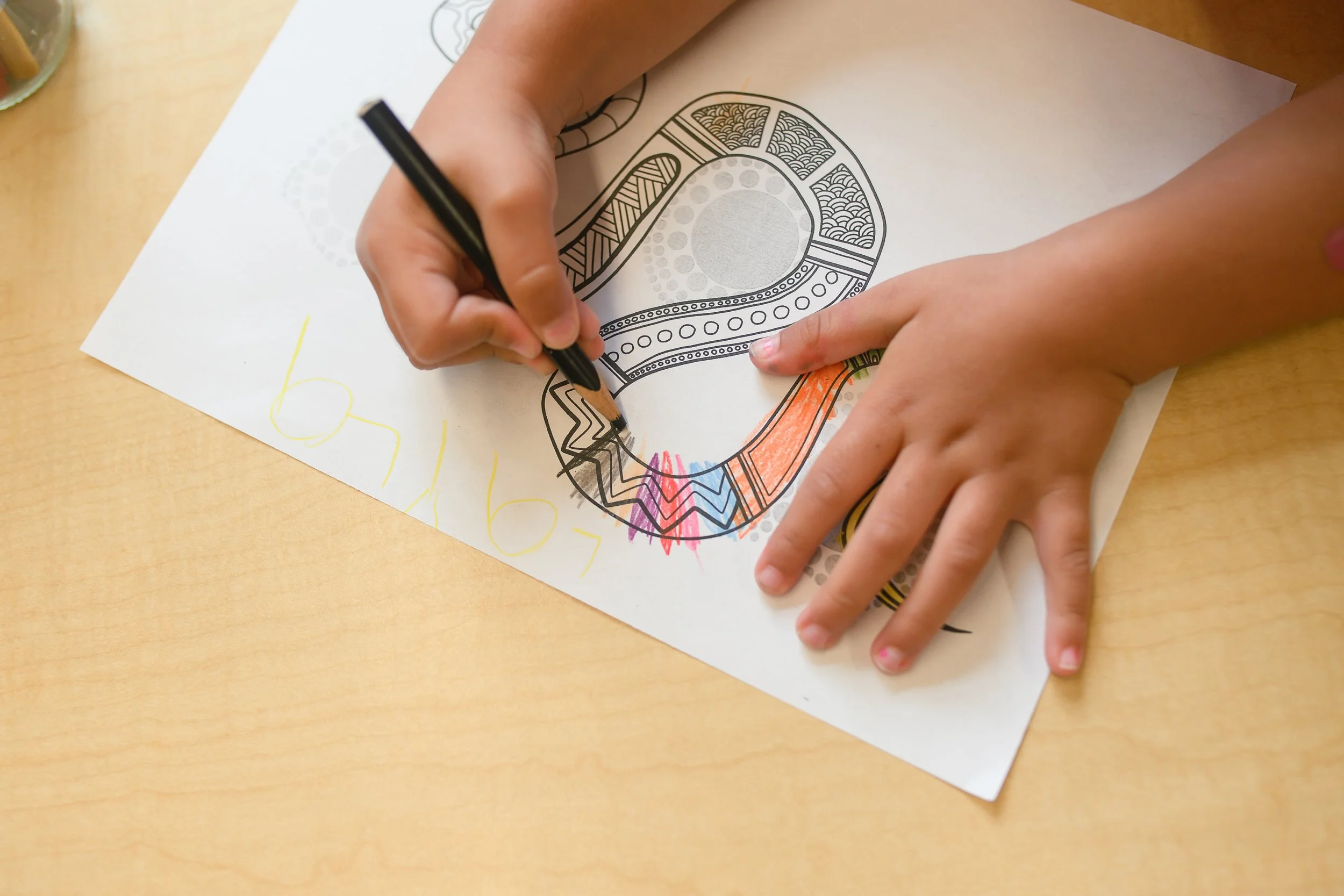 Child coloring a printed design of a crown with markers on a table.