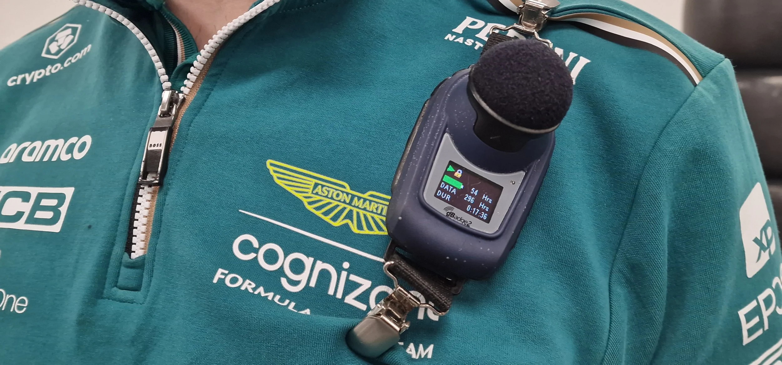 Aston Martin shirt, with a hooked sound monitoring device on person left shoulder.
