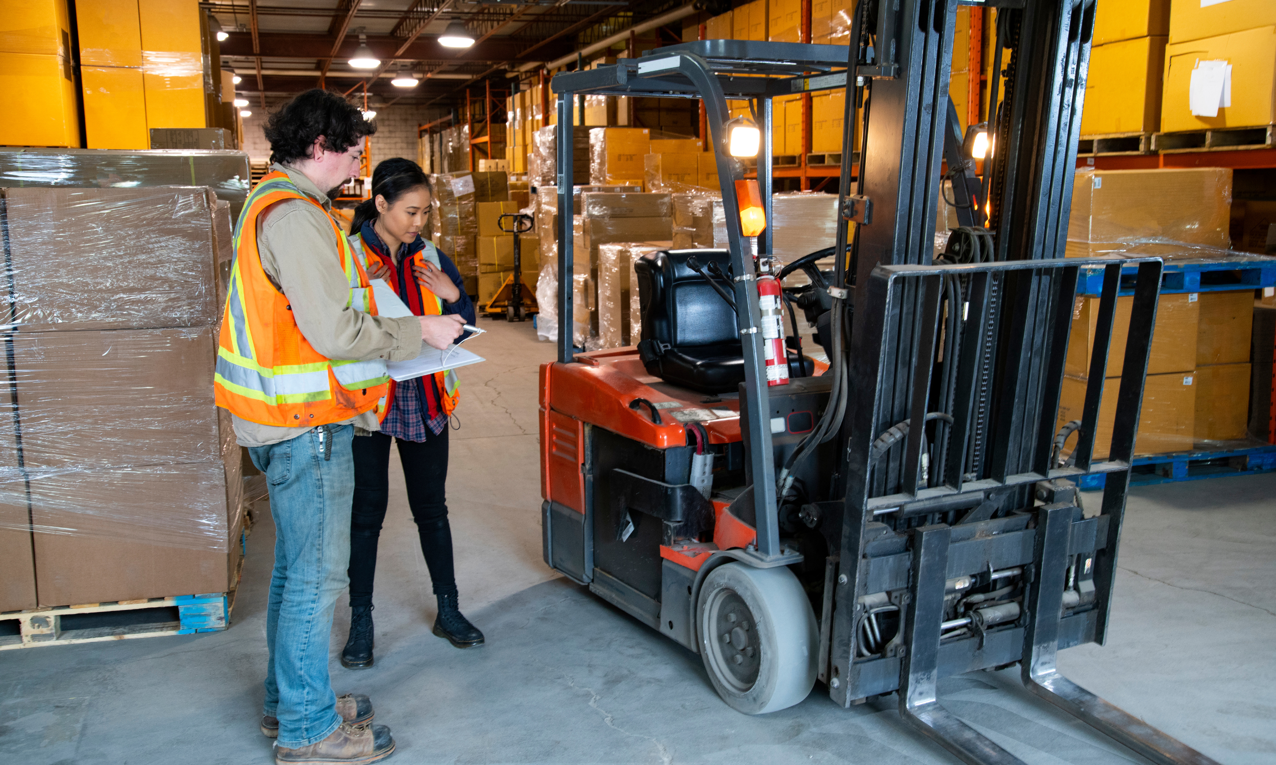 Man and Women wearing hi-vis vest in a warehouse, they are auditing a forklift before use.