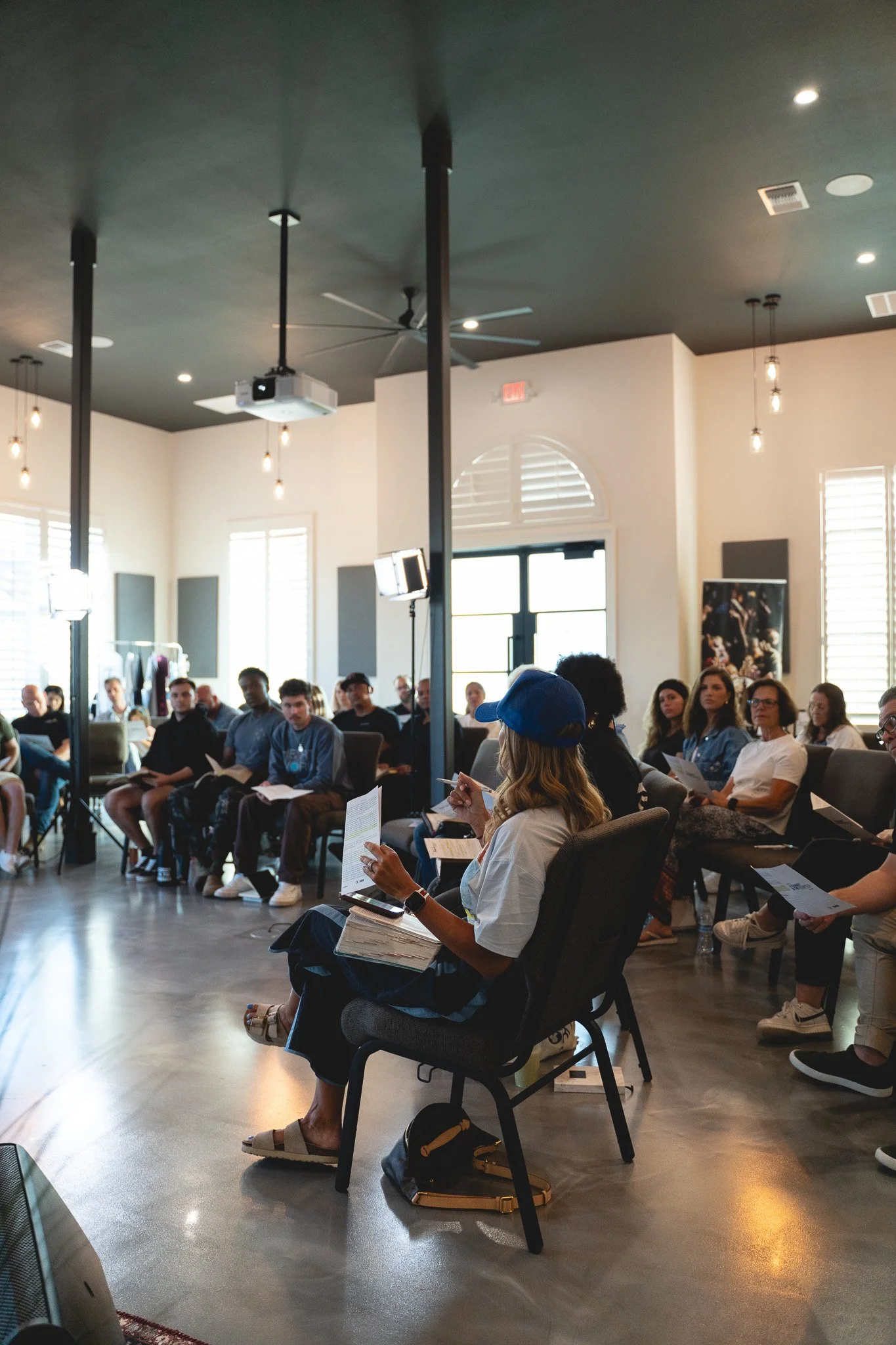 A conference room with a table set with bottled water, books, and notebooks, illuminated by sunlight filtering through blinds.