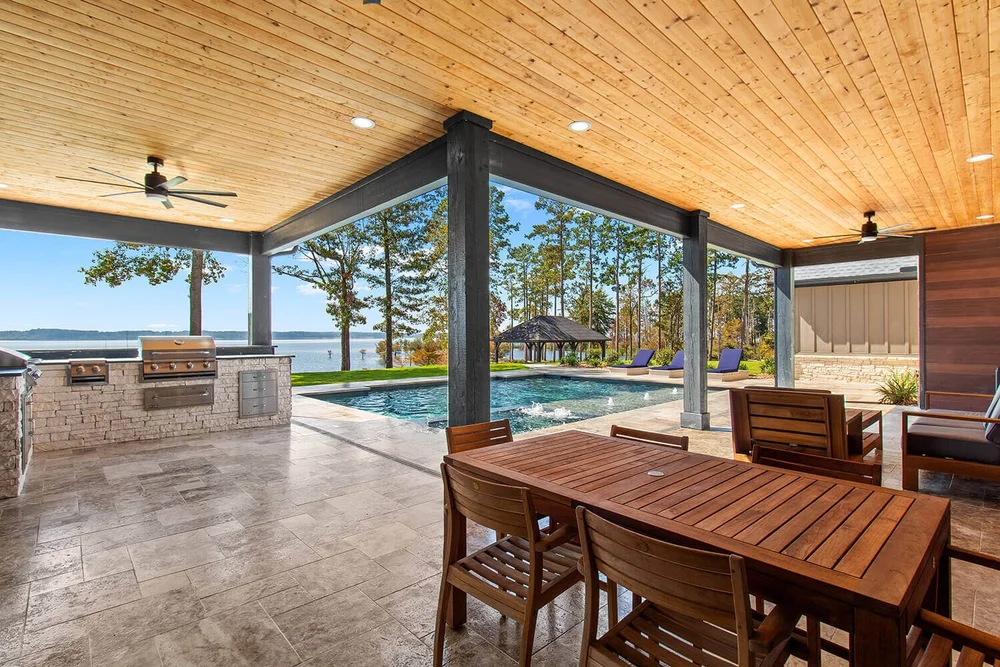 Covered outdoor pool area with ceiling fans and string lighting overlooking lake