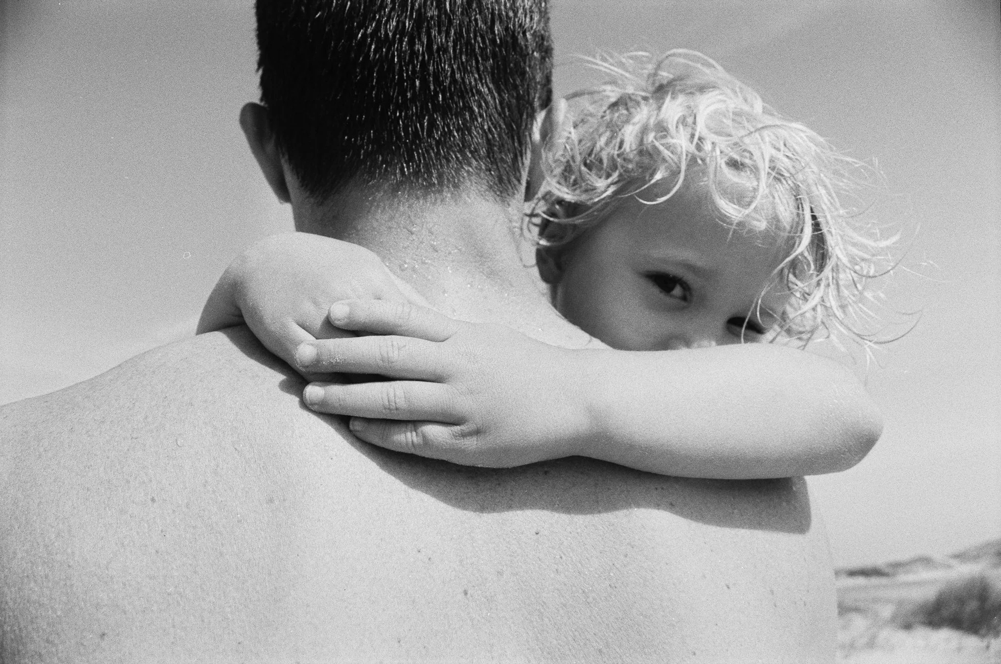 Sohn auf dem Arm des Vaters, hält sich an seiner Schulter fest – liebevoller Familienmoment