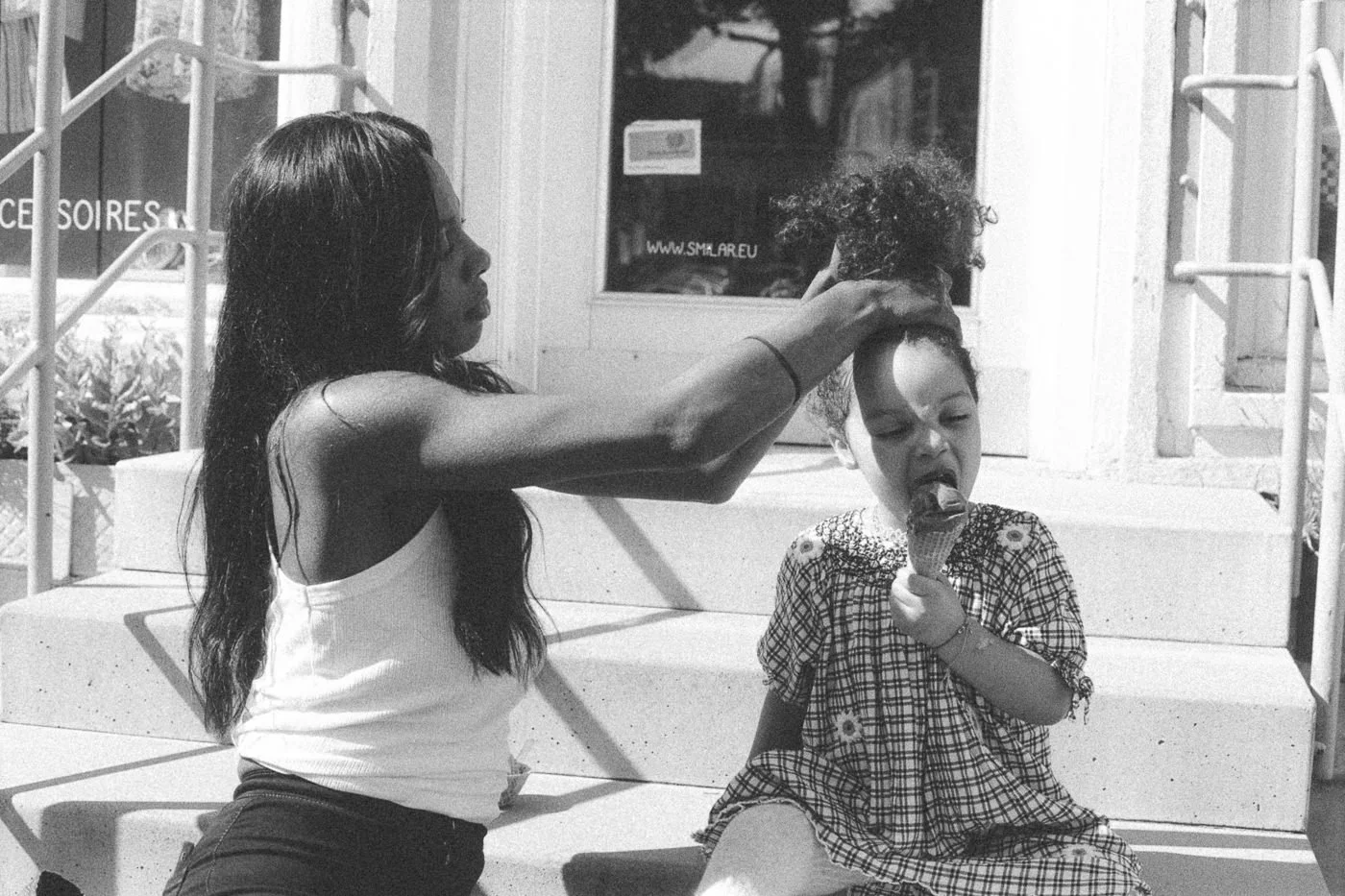 Mama bindet Tochter den Zopf beim gemeinsamen Eisessen – analoges Schwarz-Weiß Familienportrait in Mainz