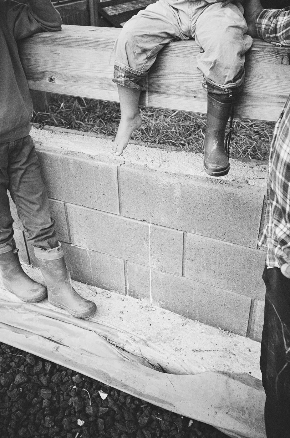Jungs sitzen wild auf einer Mauer, nur ihre Füße sichtbar – authentische analoge Schwarz-Weiß Familienfotografie in Mainz
