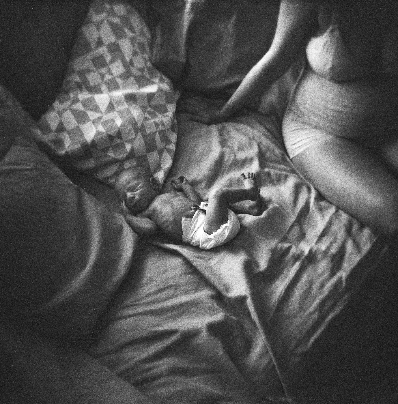 Winziges Neugeborenes liegt auf dem Bett neben der Mutter – sanfte Wochenbettaufnahme in Mainz