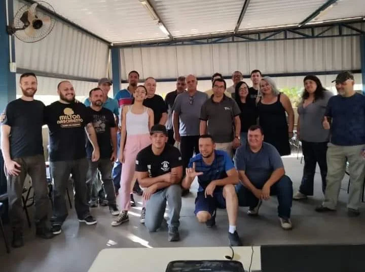 Grupo de pessoas reunido para uma foto em um galpão coberto.