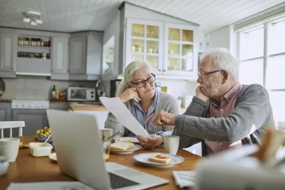 An elderly couple sitting at a kitchen table reviewing documents together.