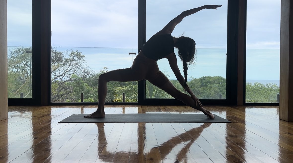 A person practicing a yoga pose indoors with an expansive window view of trees and the sky.