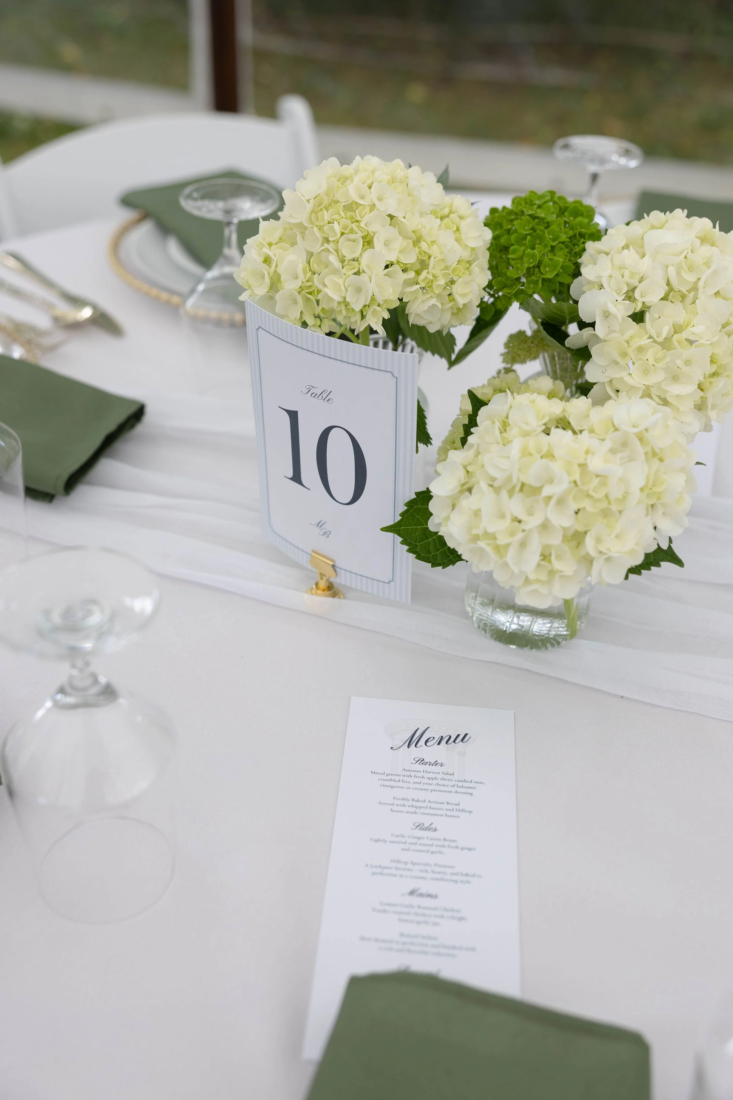 A table decorated with white and green floral arrangements, place settings, and a table number card indicating Table 10, at a formal event or wedding.
