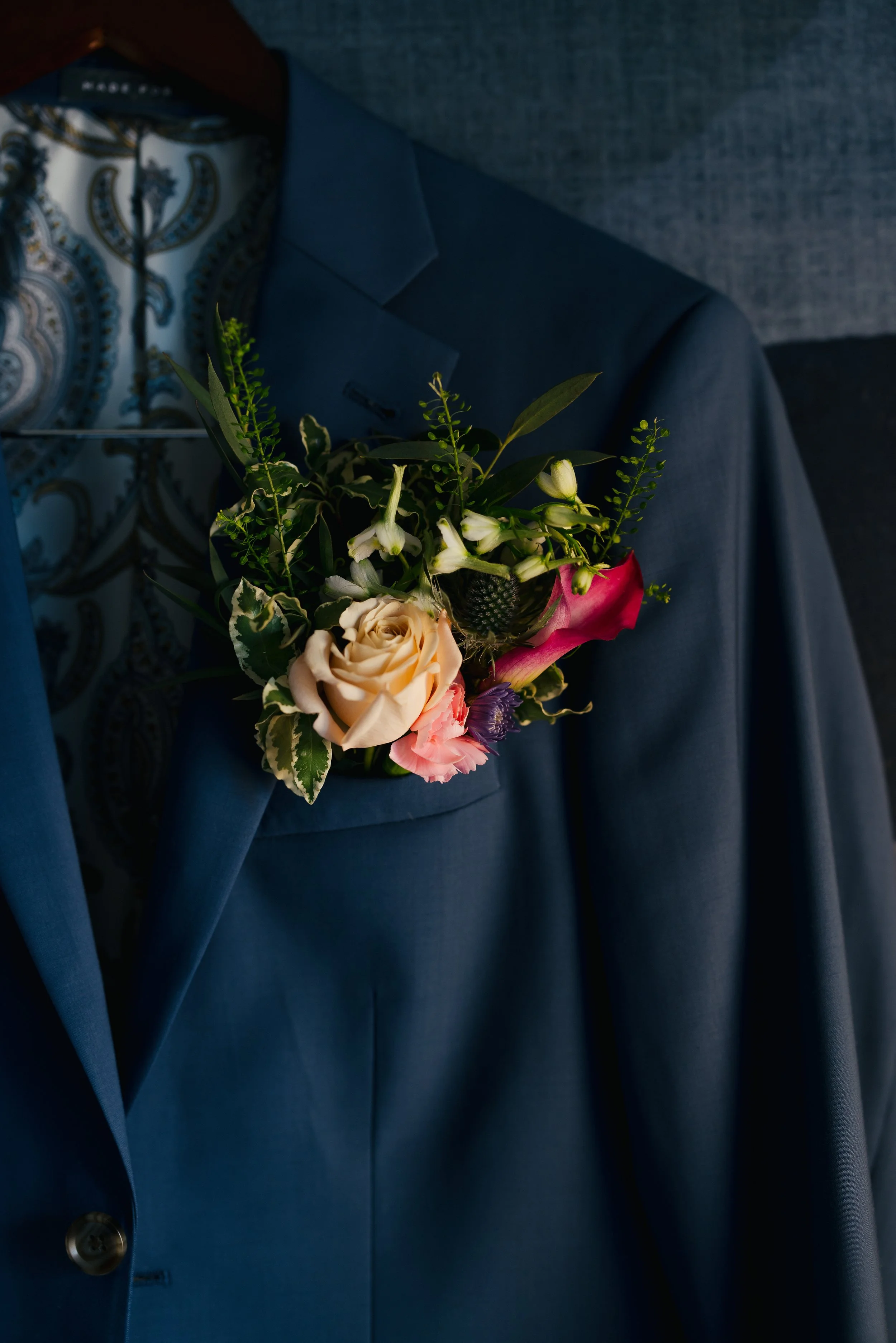 A person wearing a dark blue suit jacket and a patterned shirt holding a bouquet of flowers.