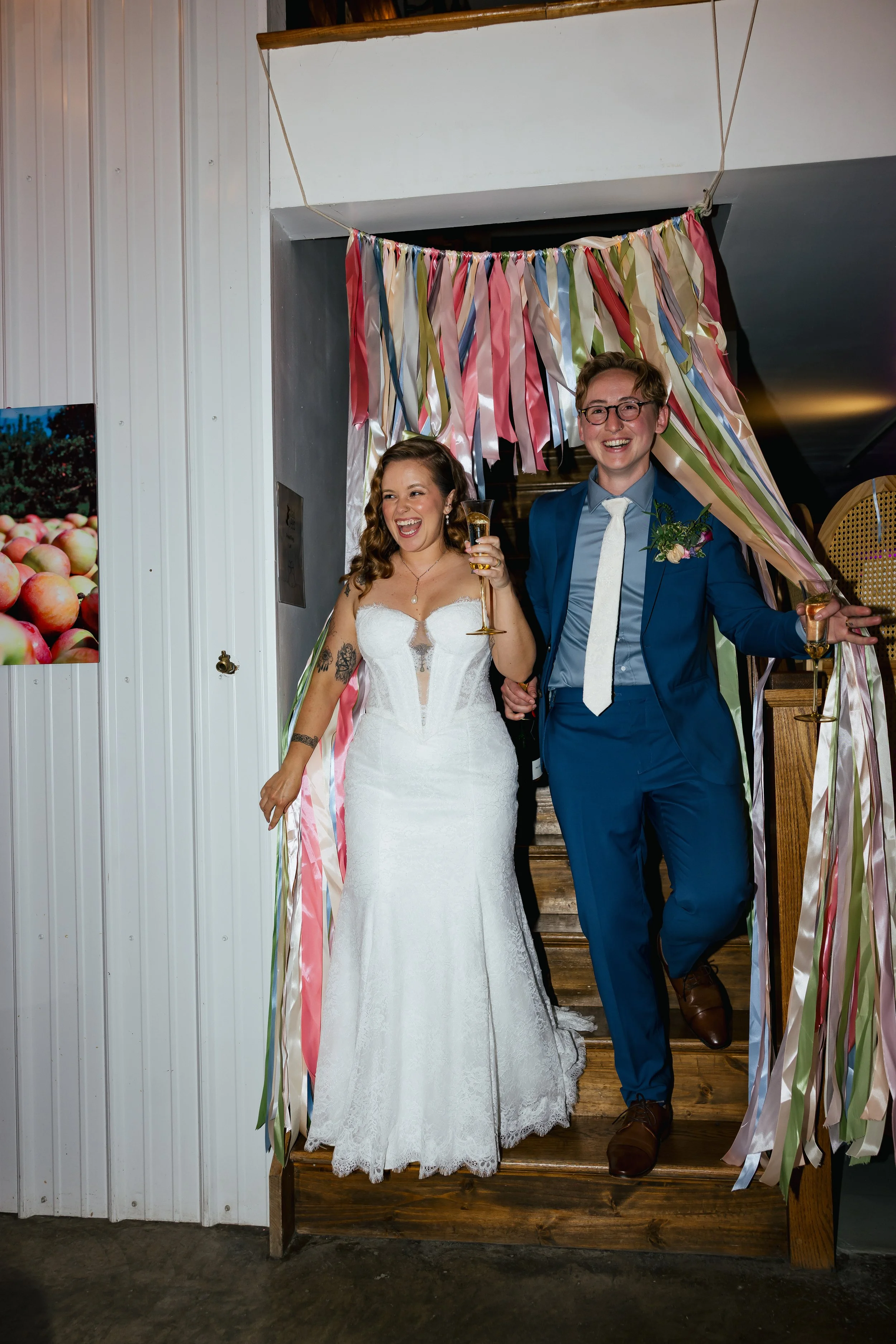 A joyful bride and groom standing under ribbons at their wedding, smiling and holding glasses of champagne.
