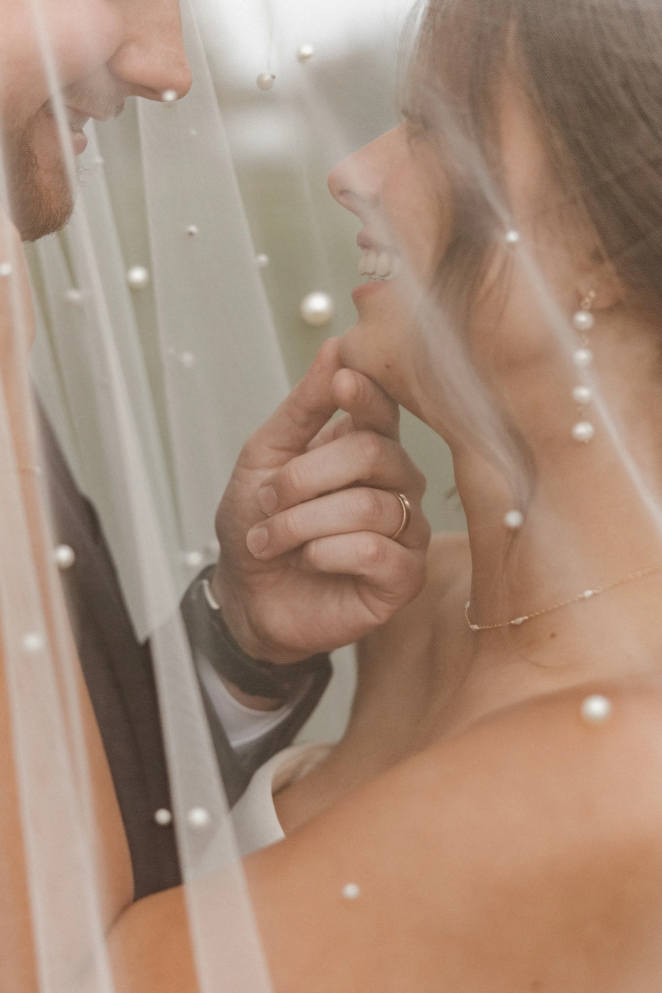 A man and woman are looking at each other through a window with white beads, close-up of their faces and necks.