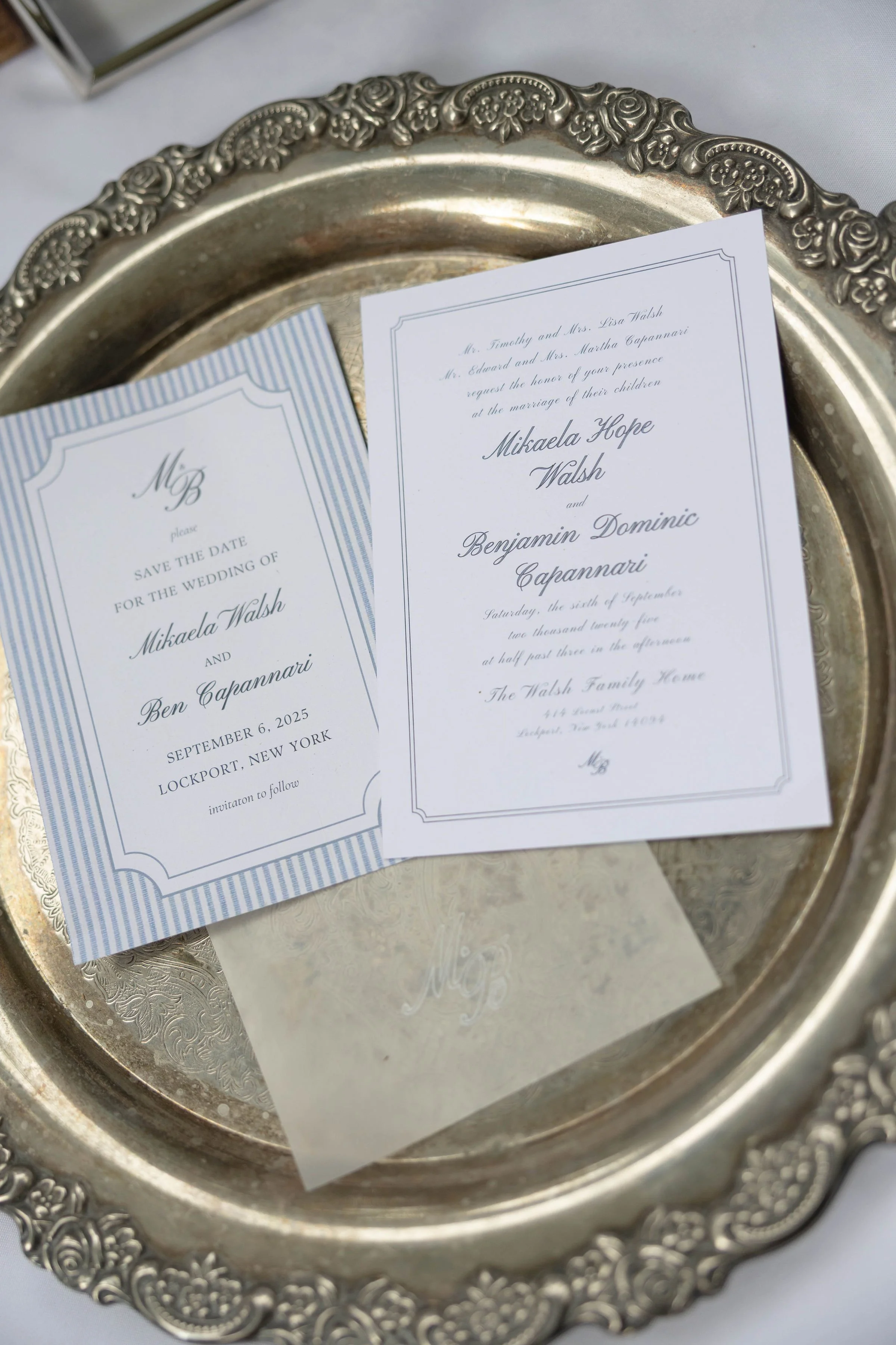 Elegant silver tray holding wedding invitation cards for Mikaela Hope Walsh and Benjamin Dominic Capannari, decorated with intricate floral patterns on the edge.
