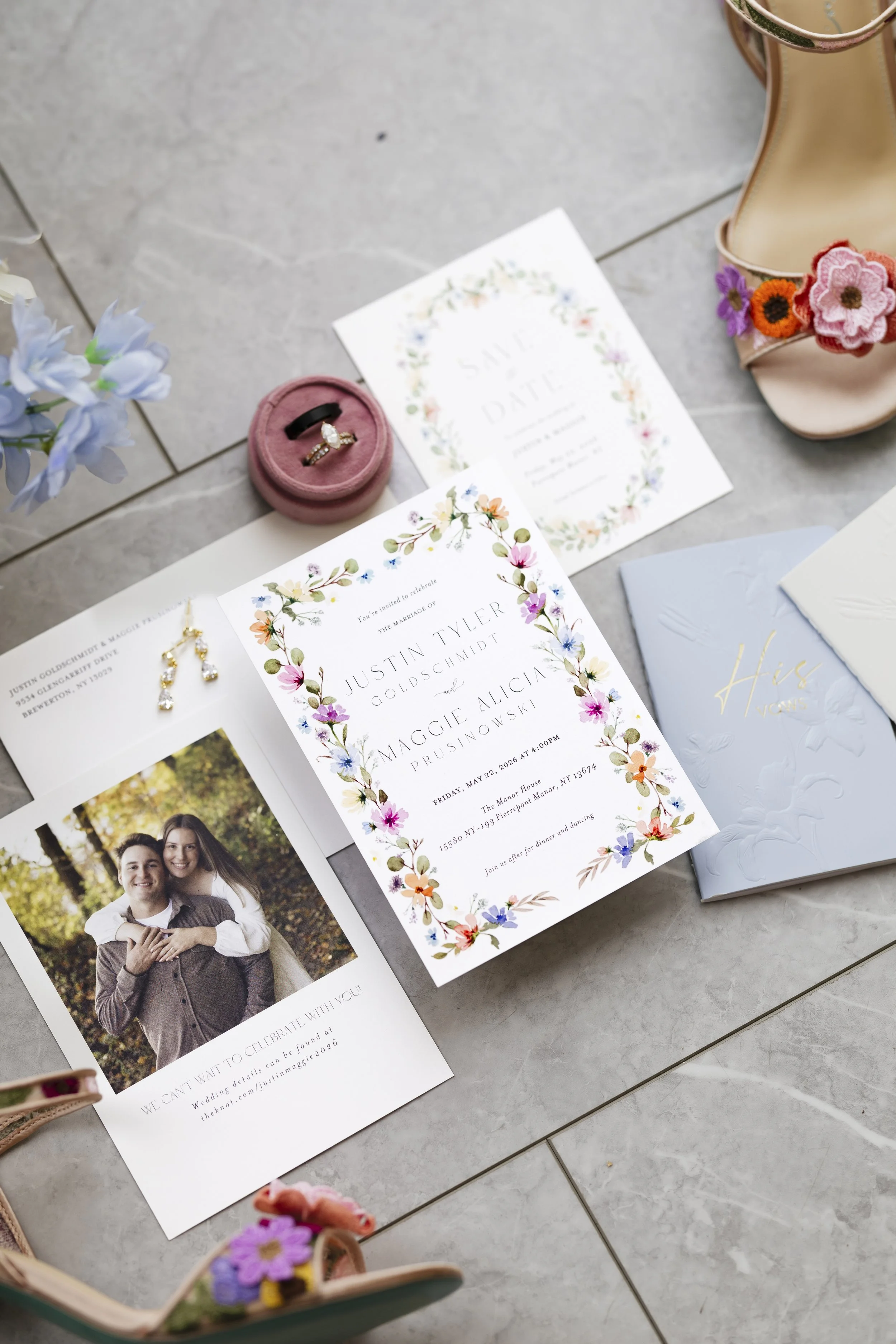 Wedding invitation and photo on tiled floor, with pink ring box, flowered high heel shoes, and pink flower decorations.