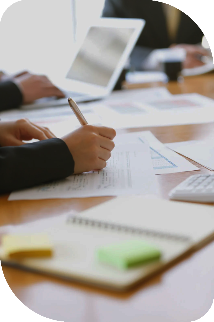 Person holding a pen and writing on documents on a wooden table.