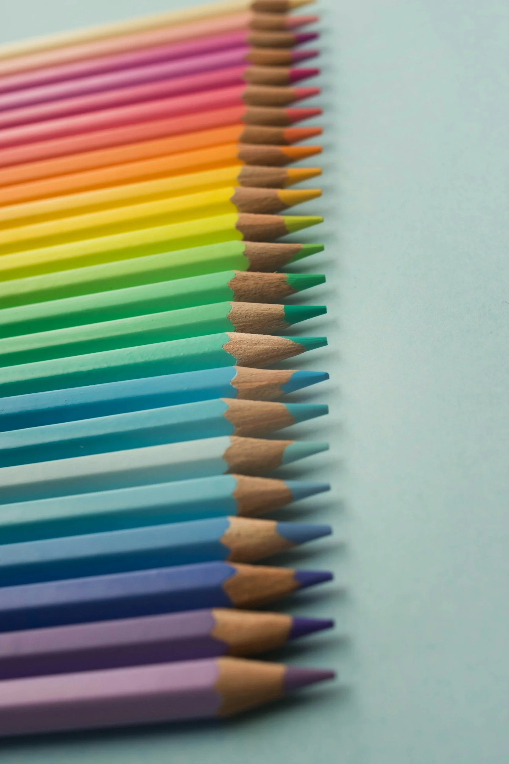 A row of colored pencils arranged in rainbow order on a light blue background.