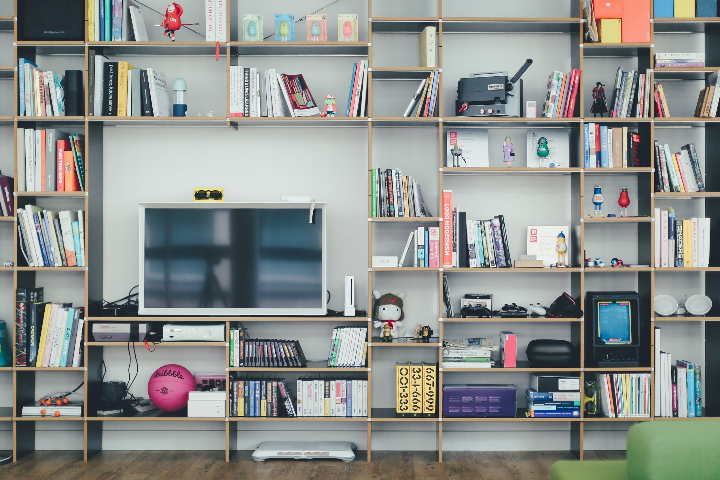 A large round shelving unit filled with books, toys, electronic devices, and decorative items, with a flat-screen TV mounted on the middle shelf.