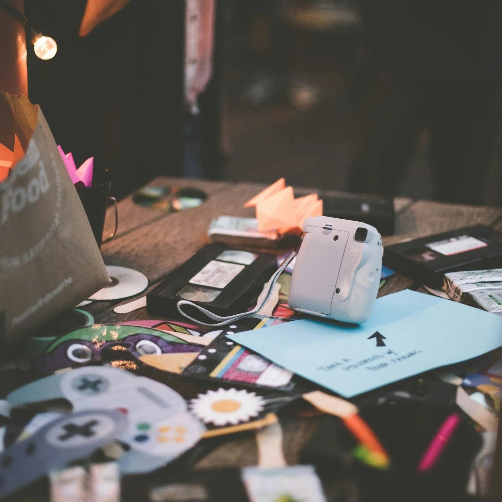 Messy cluttered workspace with various colorful paper notes, a digital camera, and a sheet of paper with an arrow pointing up.