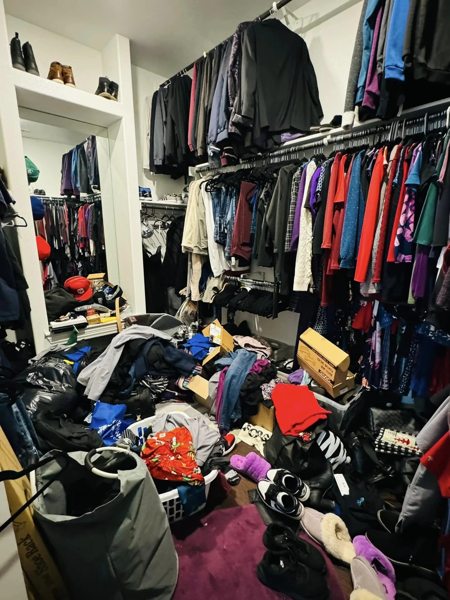 Cluttered walk-in closet with clothing, shoes, and boxes scattered on the floor and hanging on racks.