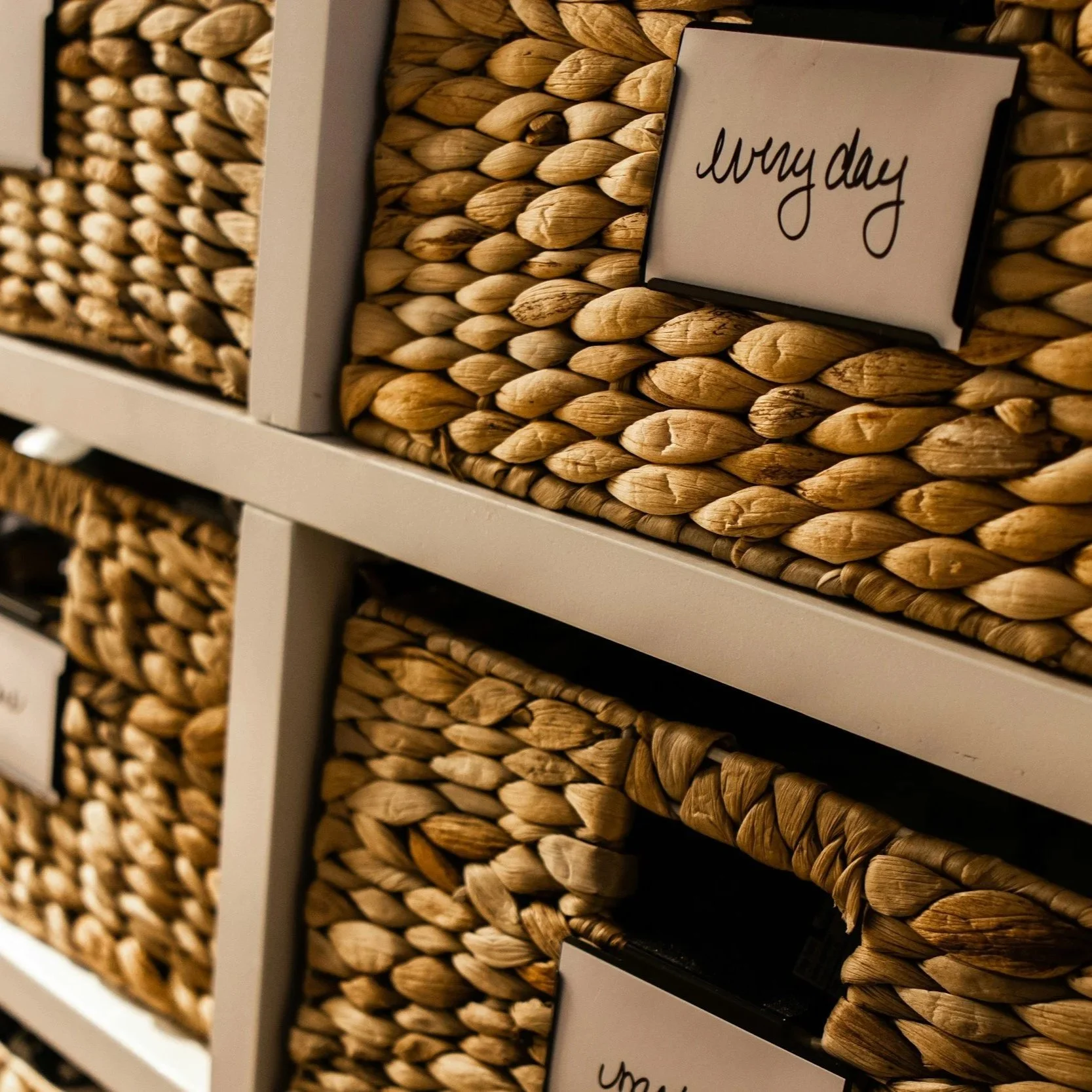 Close-up of woven storage baskets on white shelves with a sign that says "every day".