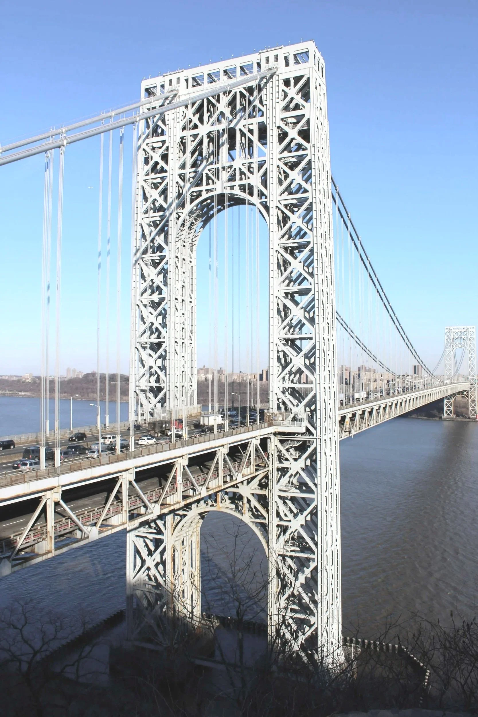 A large white suspension bridge spanning a river with a view of the city skyline in the background.